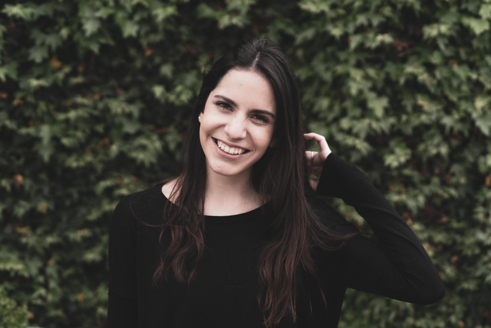A woman in a black shirt is smiling and touching her hair.
