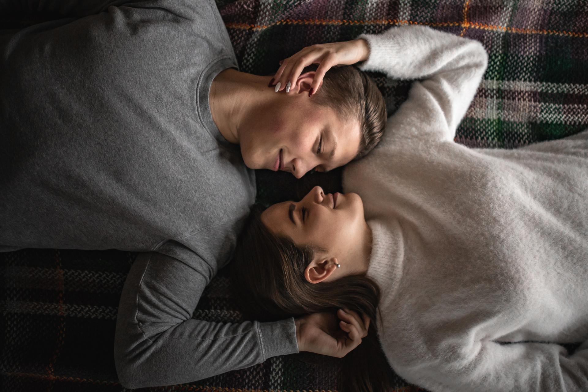 A man and a woman are laying on a blanket and looking at each other.