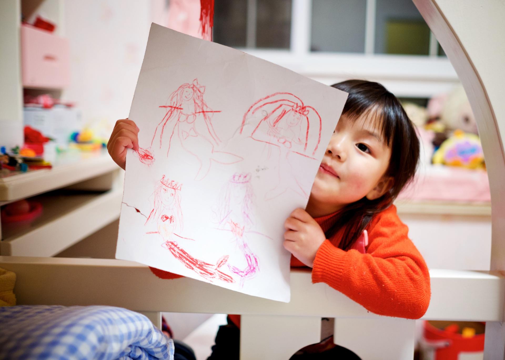 A little girl is holding a piece of paper with a drawing on it.
