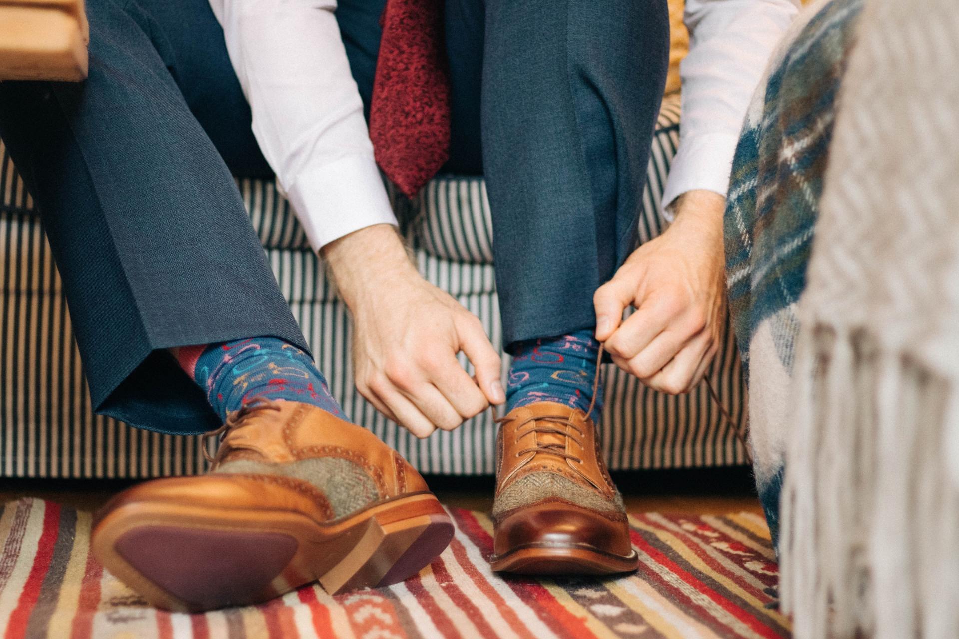 Two people sit on a couch, adjusting tan leather shoes over colorful patterned socks.