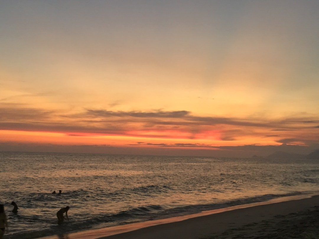 Um pôr do sol sobre o oceano com pessoas em pé na praia.