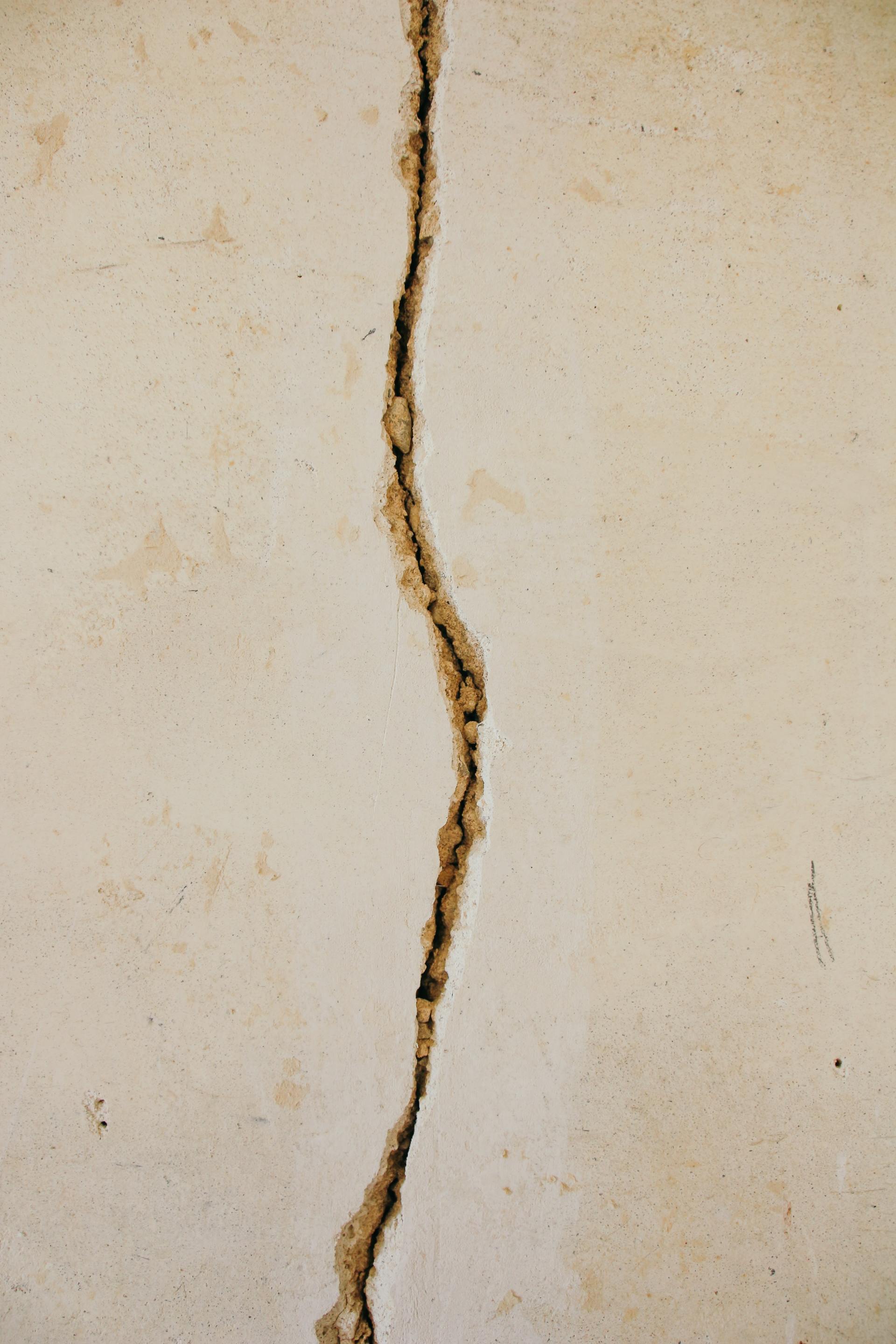 Close-up of a light-colored wall with a long, vertical crack filled with dark material.