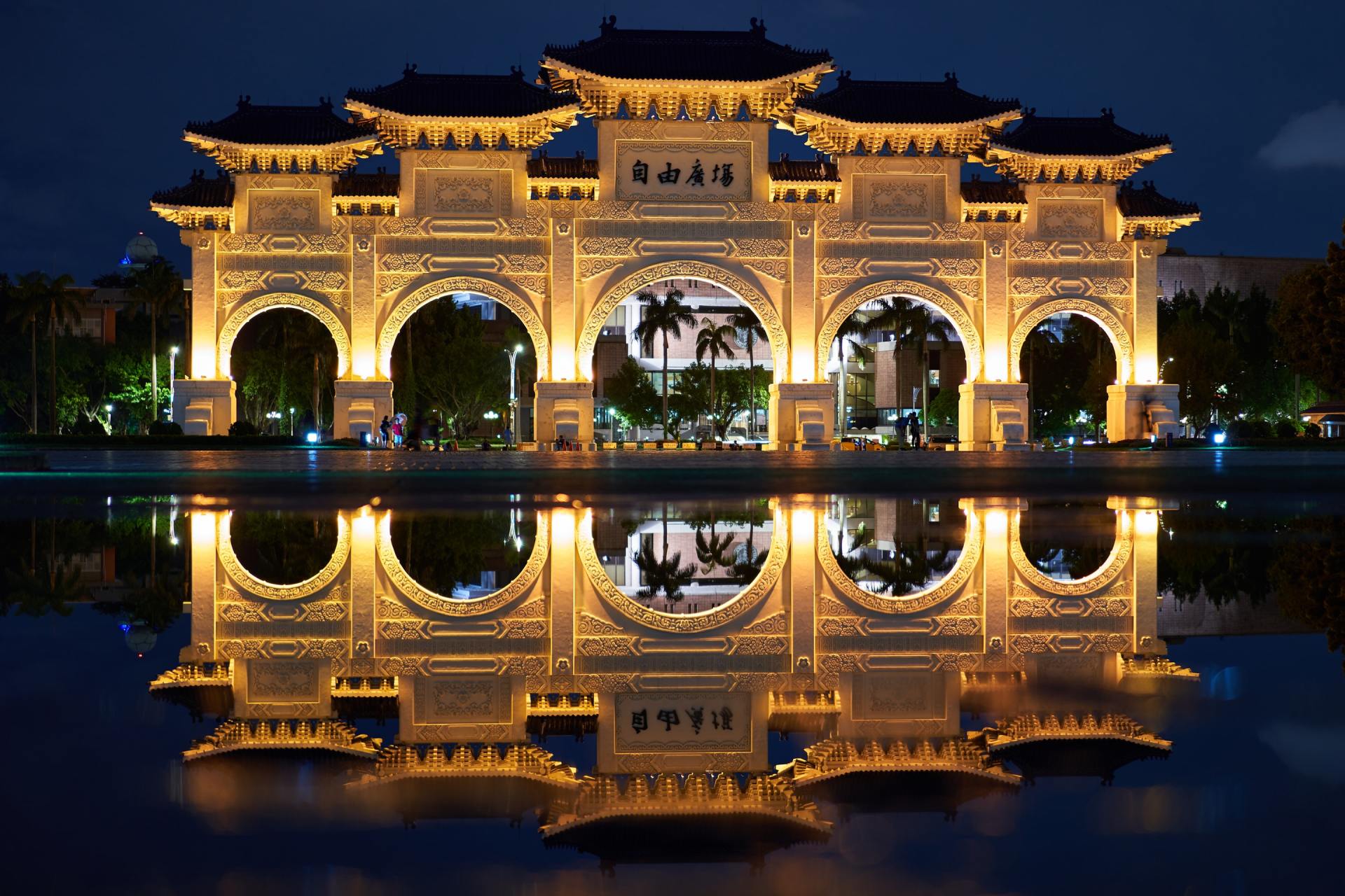 Illuminated ornate arch reflected in water at night in Taipei, Taiwan.