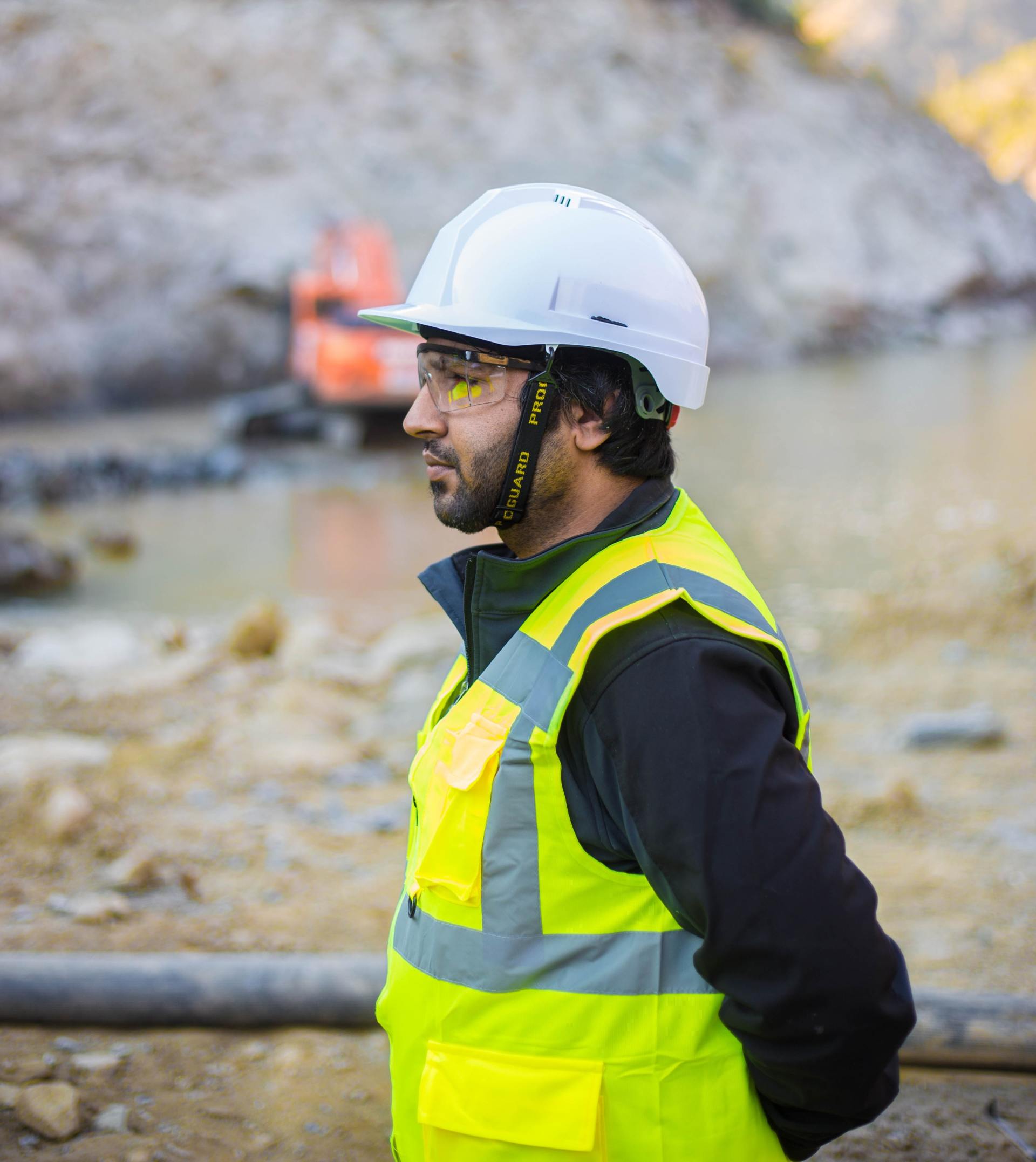A man wearing a hard hat and safety vest is standing on a construction site.