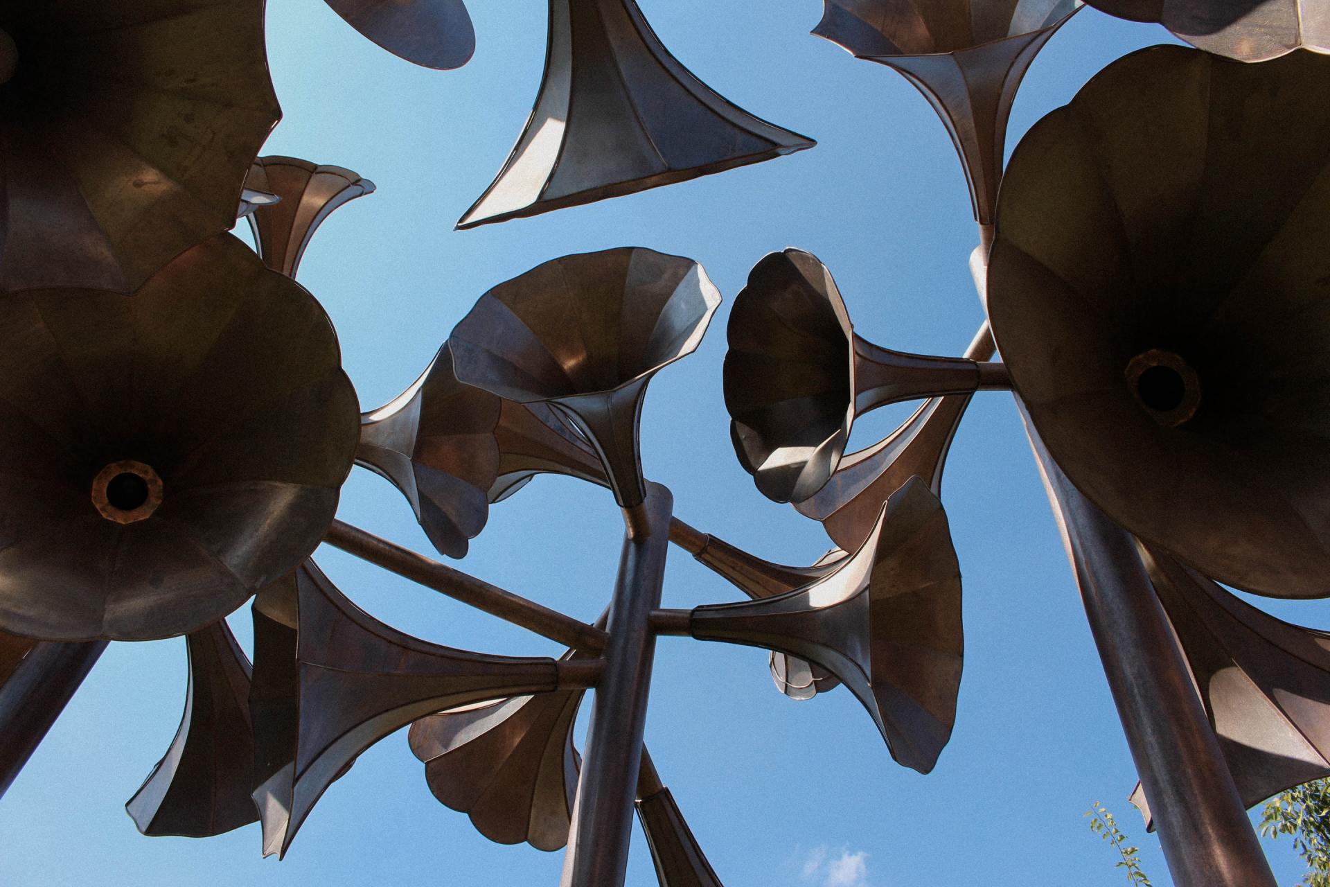 Low-angle view of dark megaphone or speaker-shaped silhouettes against a bright blue sky, creating a pattern that suggests broadcasting or amplifying messages.