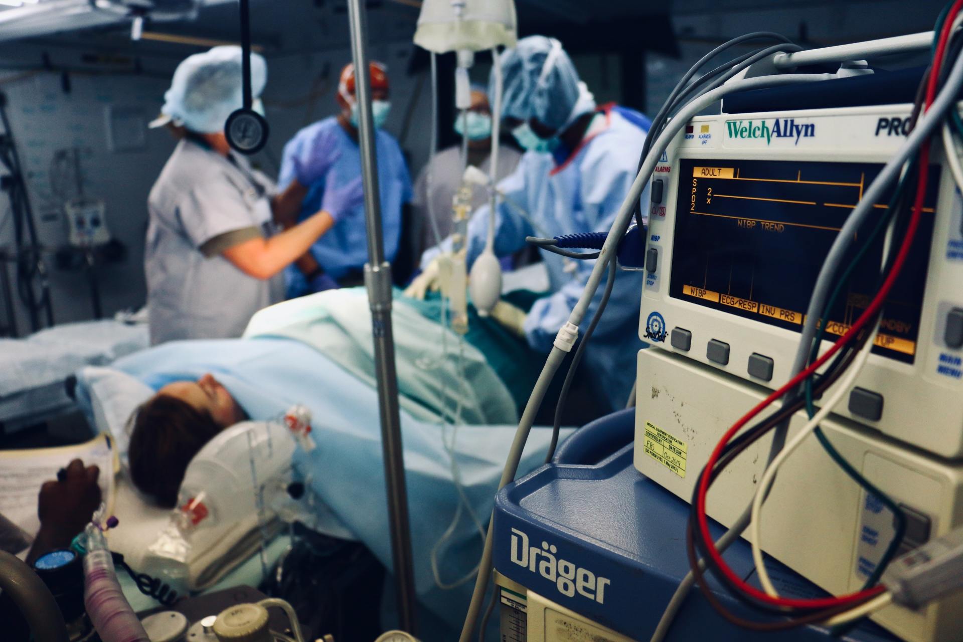Patient in operating room with medical staff. Vital signs monitor in foreground.