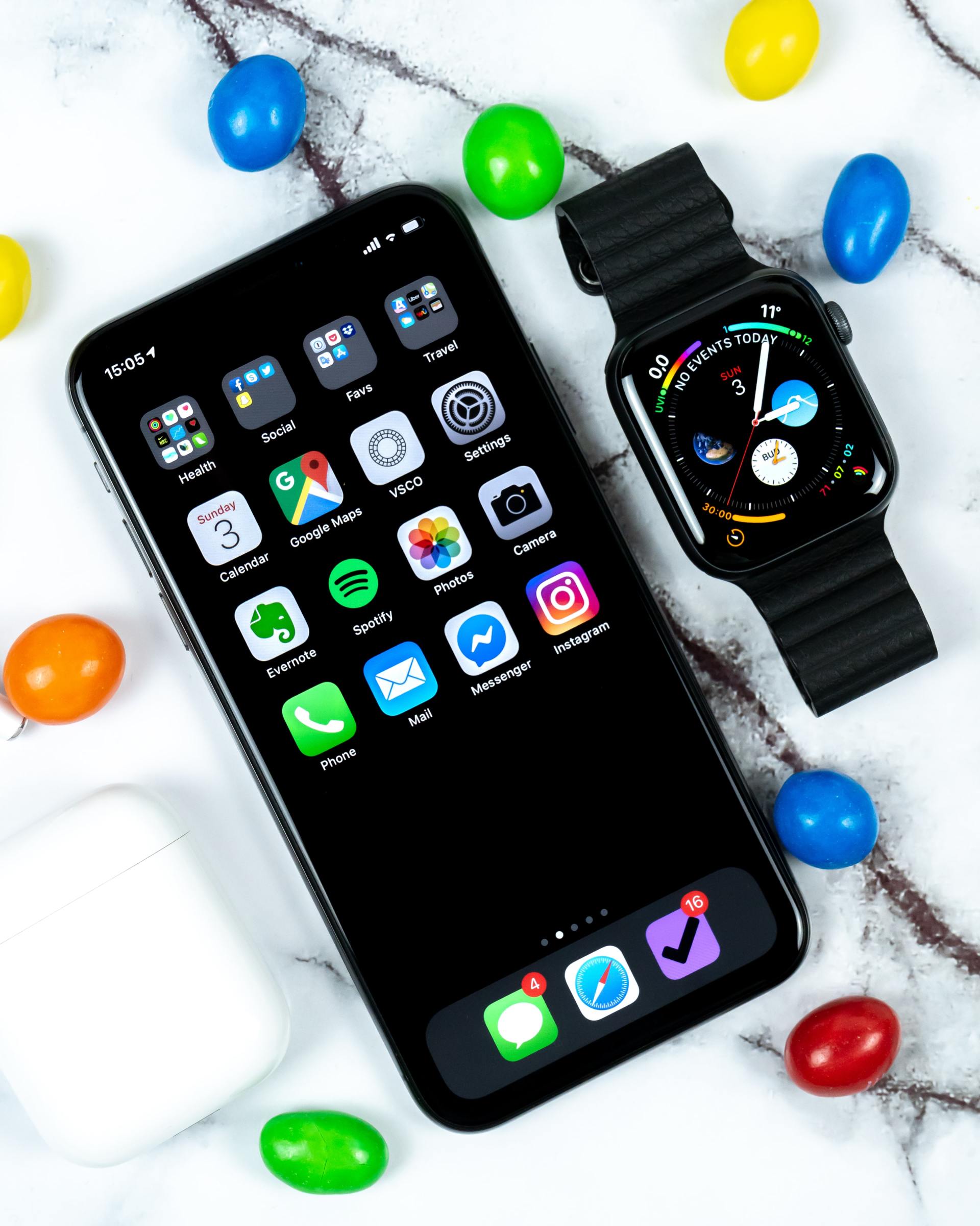 A smart phone and a smart watch are on a table surrounded by candy.