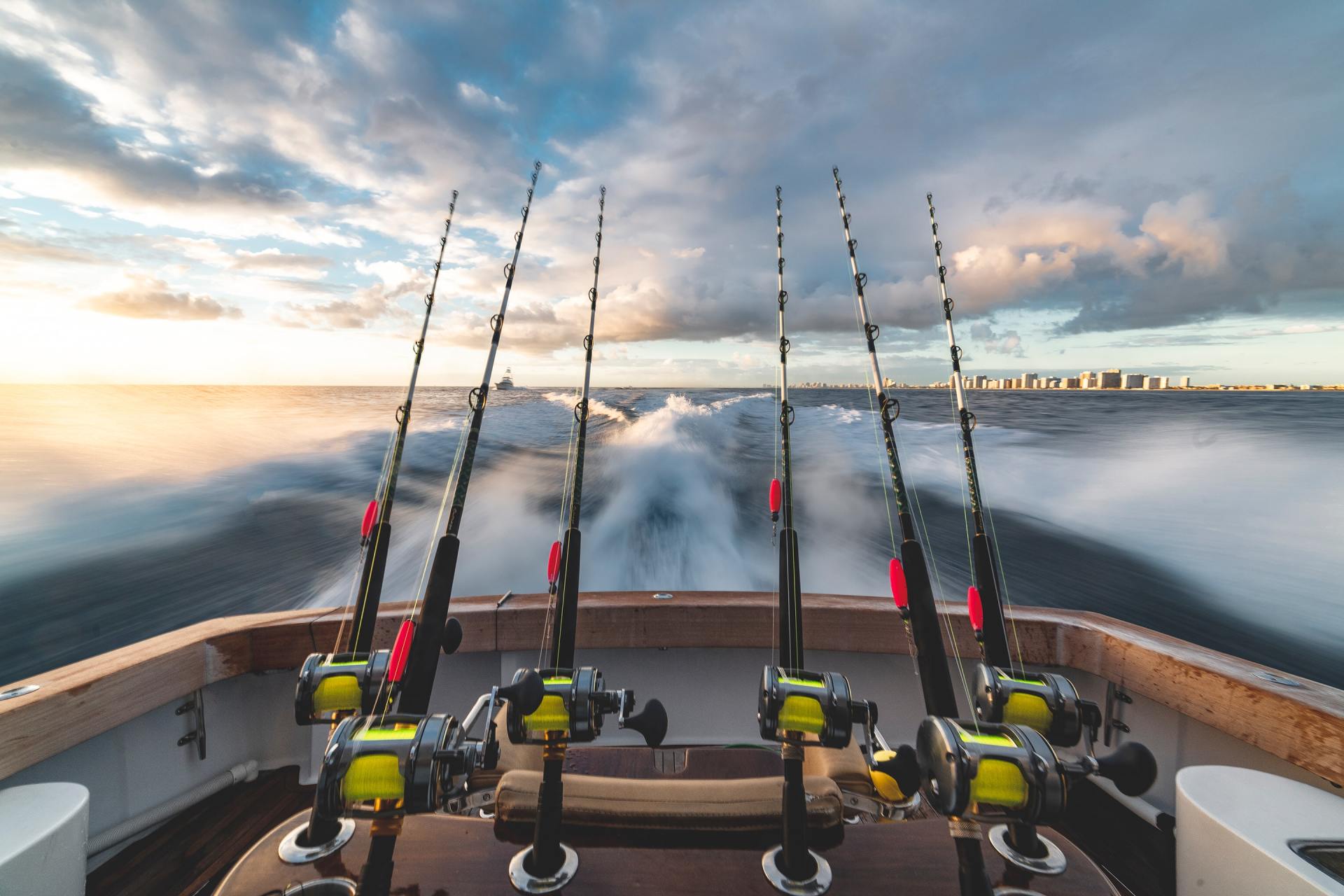 Fishing rods mounted on a boat speeding across the water at sunset.