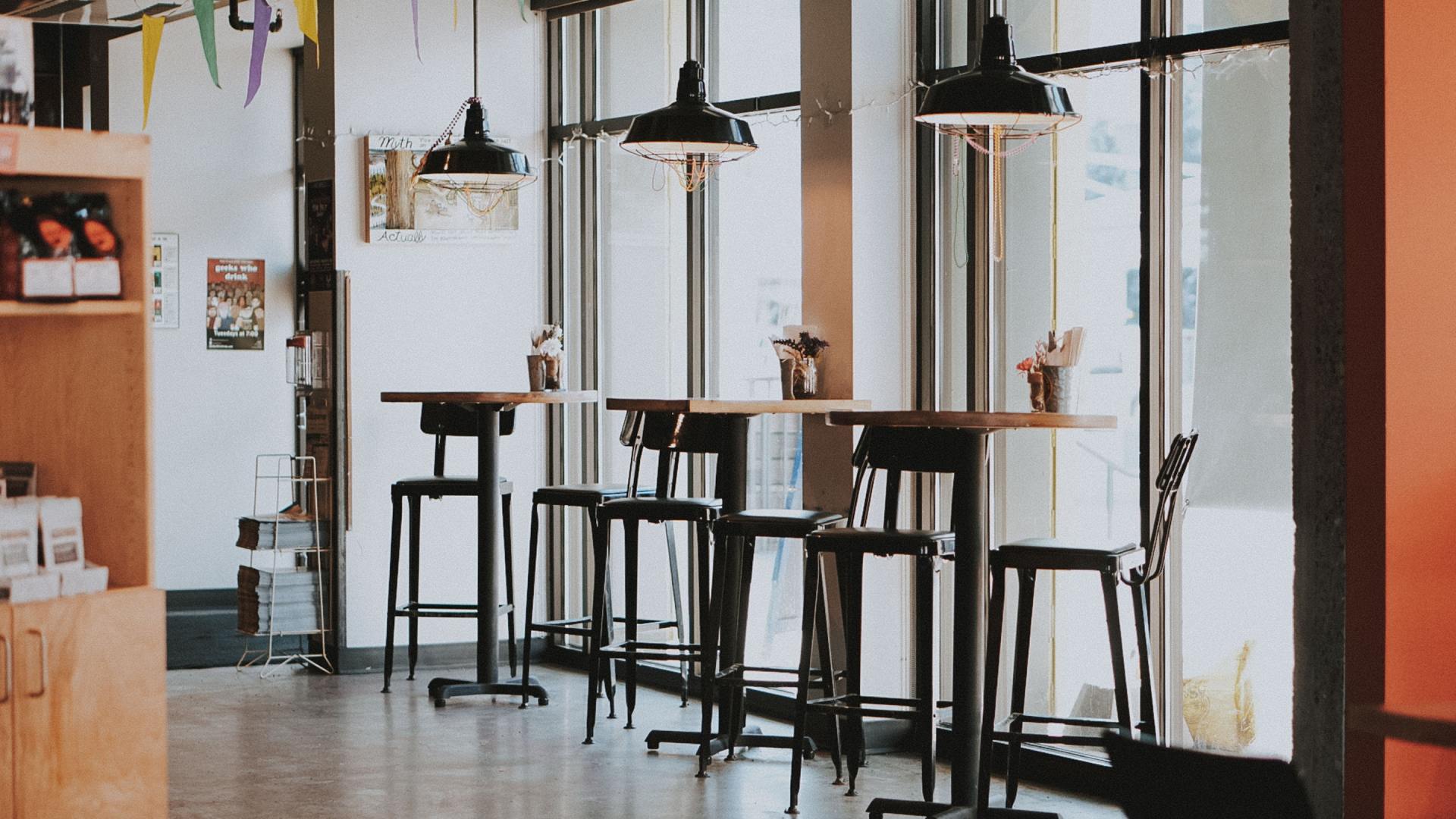 In un caffè luminoso e moderno, tavoli alti e sgabelli vuoti sono allineati lungo le grandi finestre.