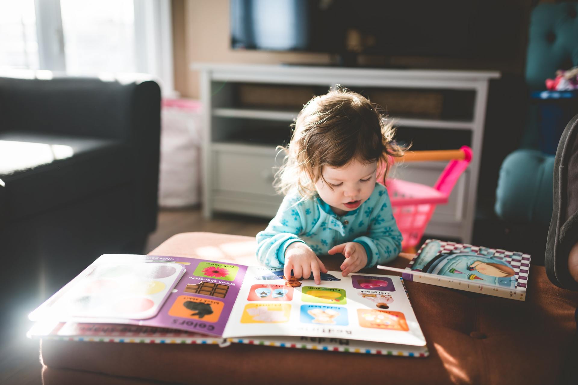 A little girl is sitting at a table reading a book.