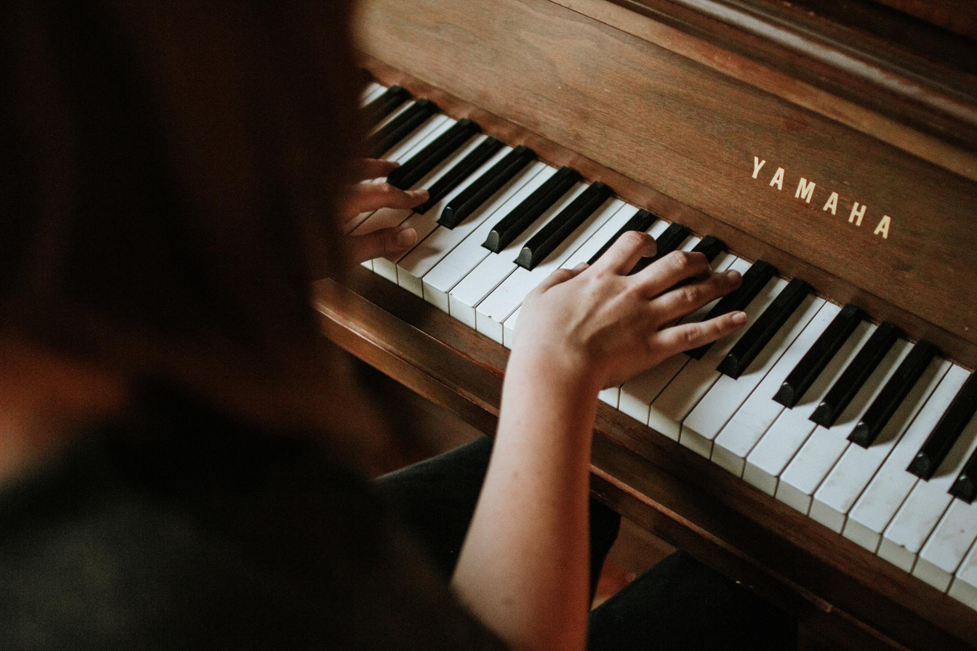 A person playing a wooden Yamaha piano. Focus on hands on keys. Brown and white keys, indoors.