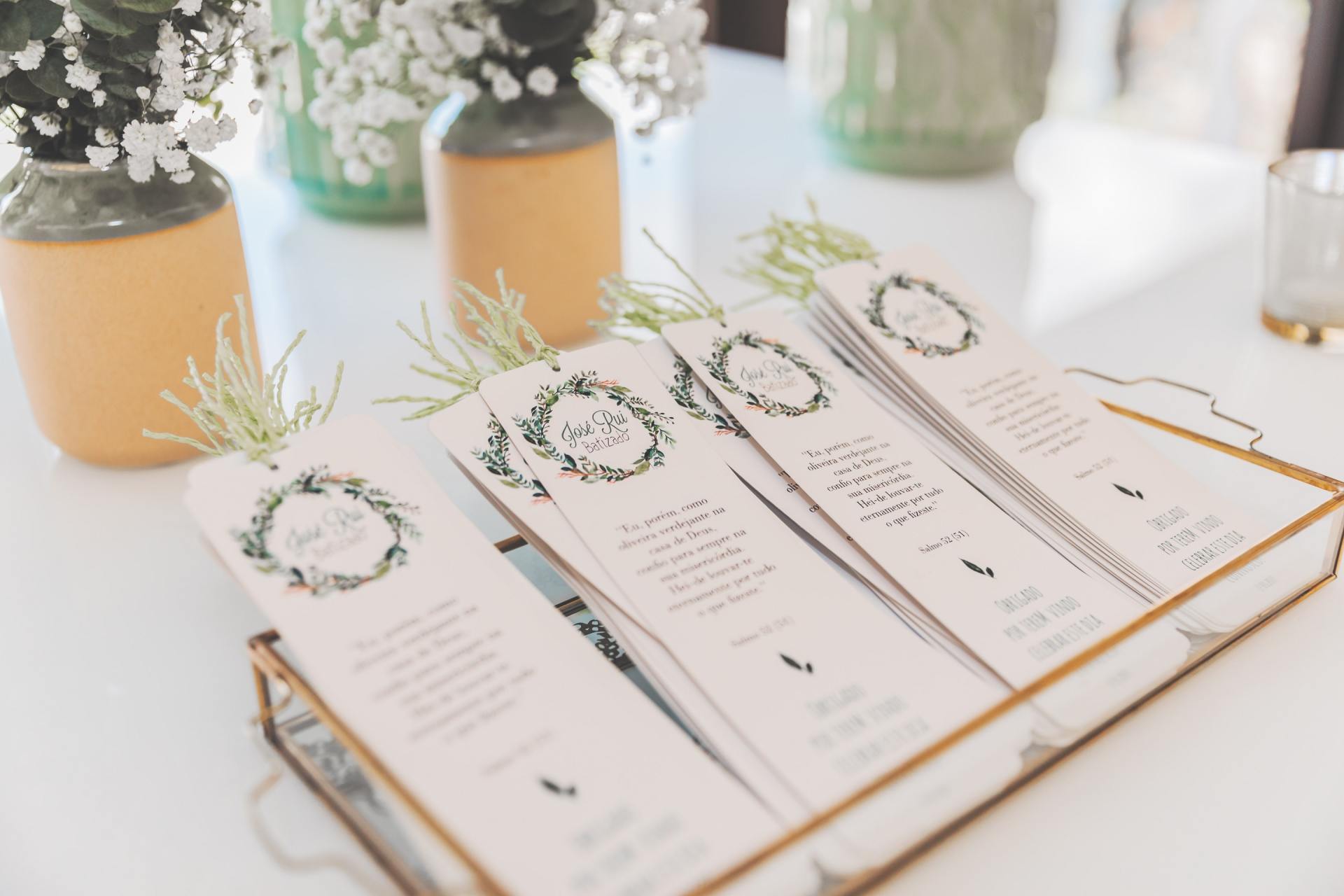 Bookmarks with greenery in a tray, next to vases with flowers.