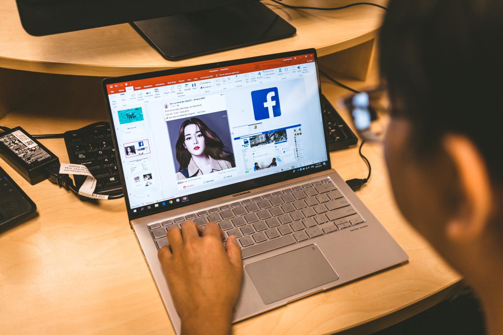 A person is typing on a laptop with a facebook logo on the screen