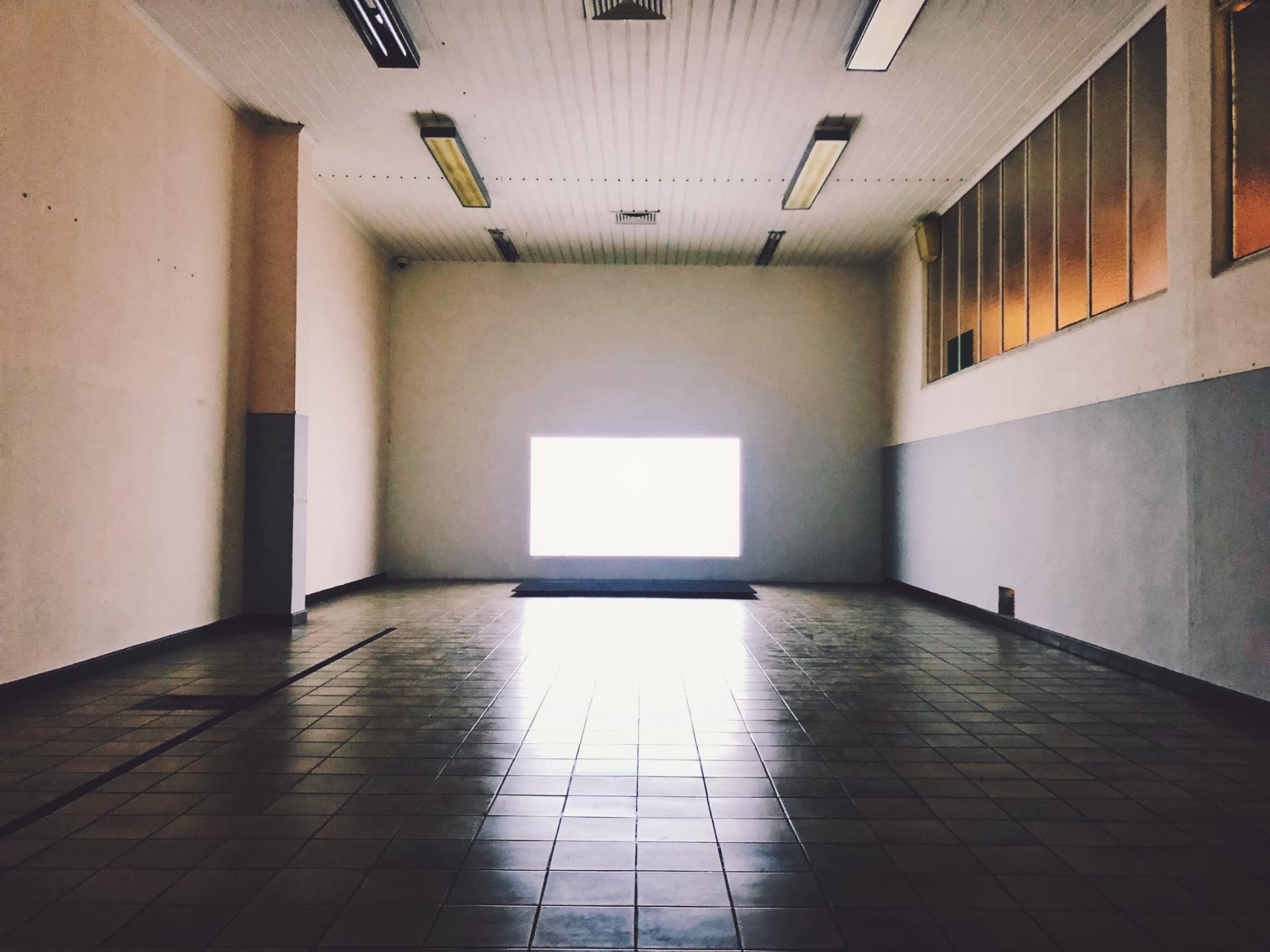 Empty tiled room with white walls and a bright window at the far end