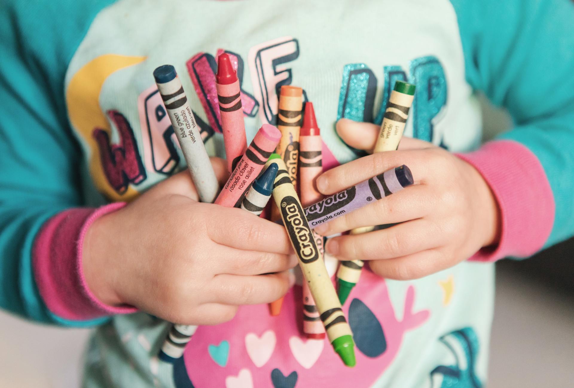A child is holding a bunch of crayons in their hands.