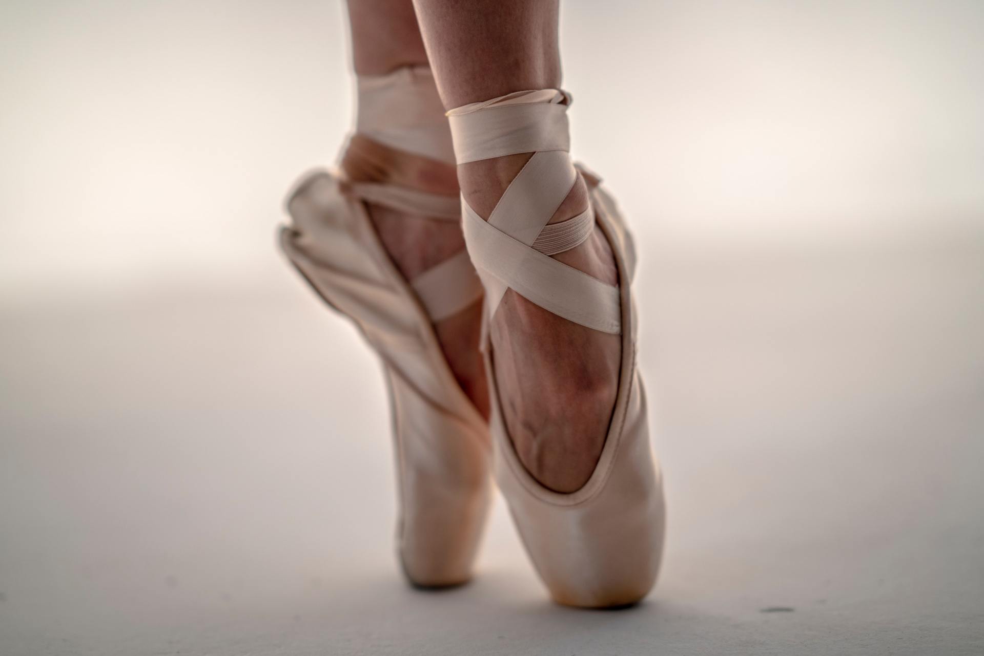 Ballet dancer's feet in pink pointe shoes, en pointe on a white surface.