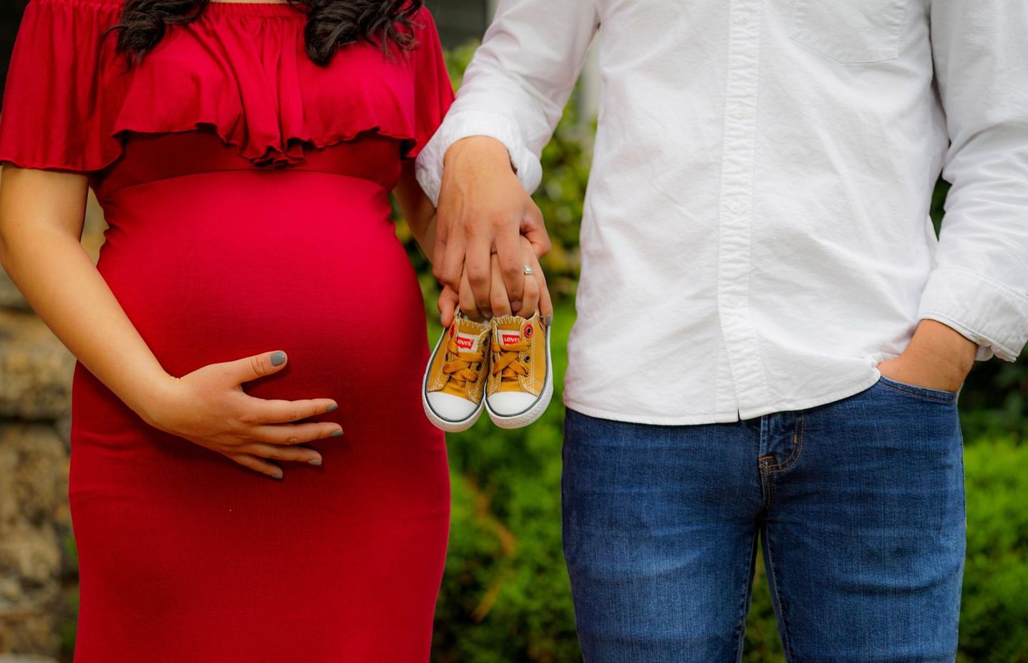 A pregnant woman is holding a pair of baby shoes next to a man.