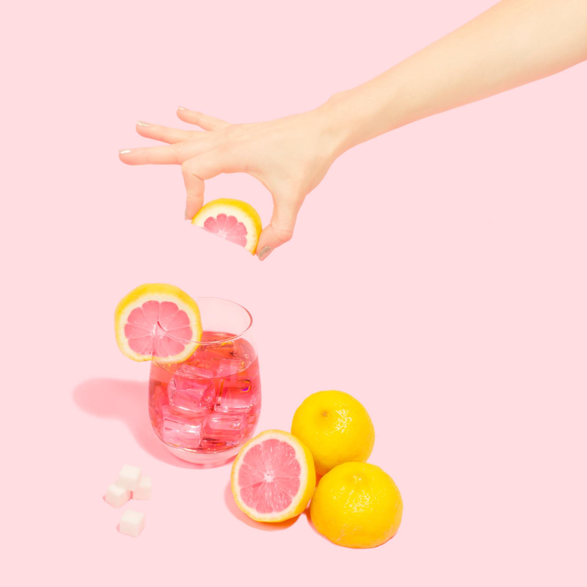 Une main tient une tranche de pamplemousse au-dessus d'un verre de limonade rose.