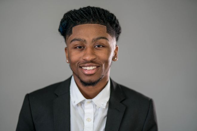 A young man in a suit and white shirt is smiling for the camera.