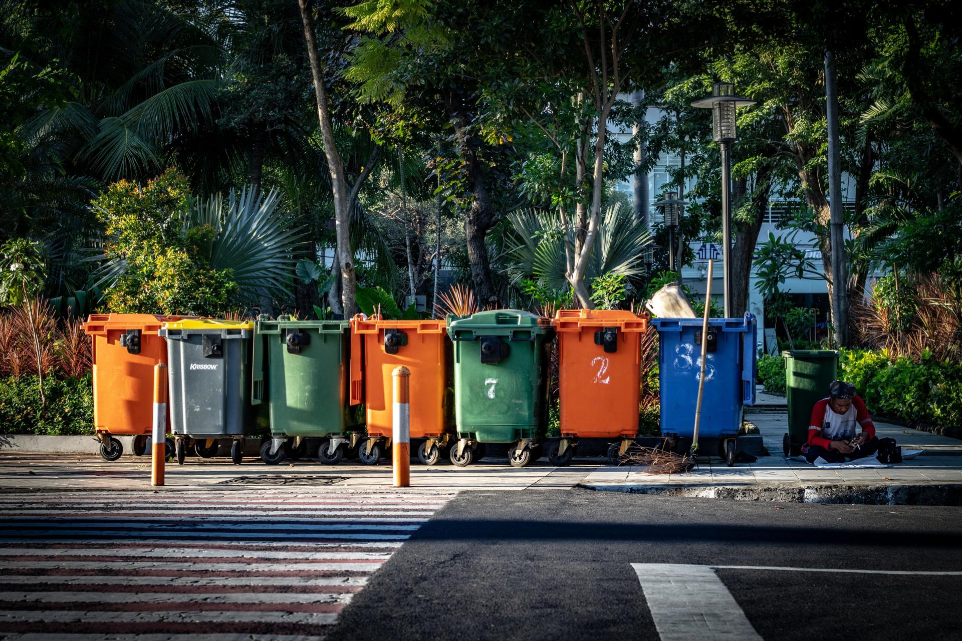 A row of colorful trash cans are parked on the side of the road.