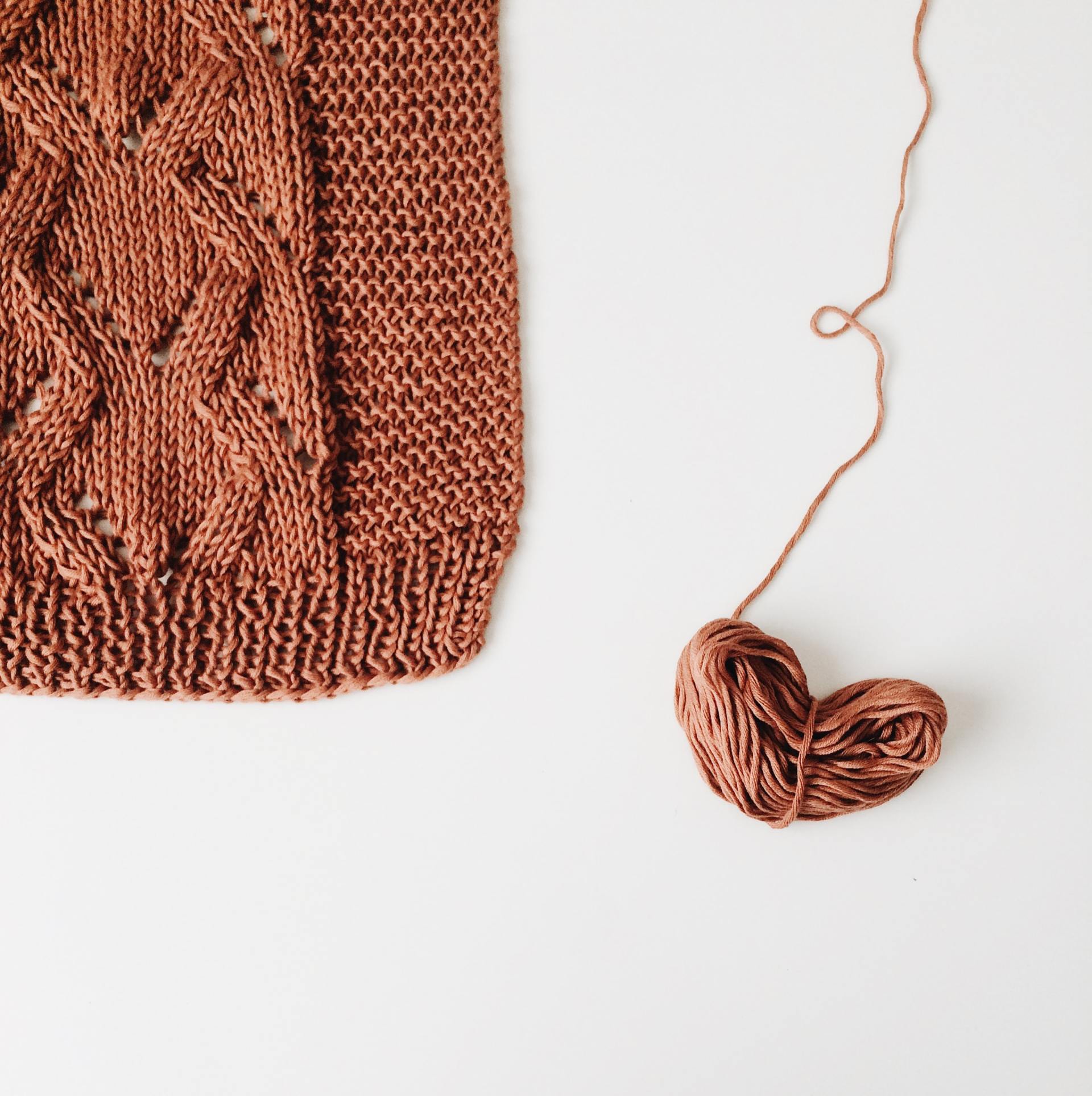 Brown knitted fabric swatch with cable pattern and a ball of yarn on a white background