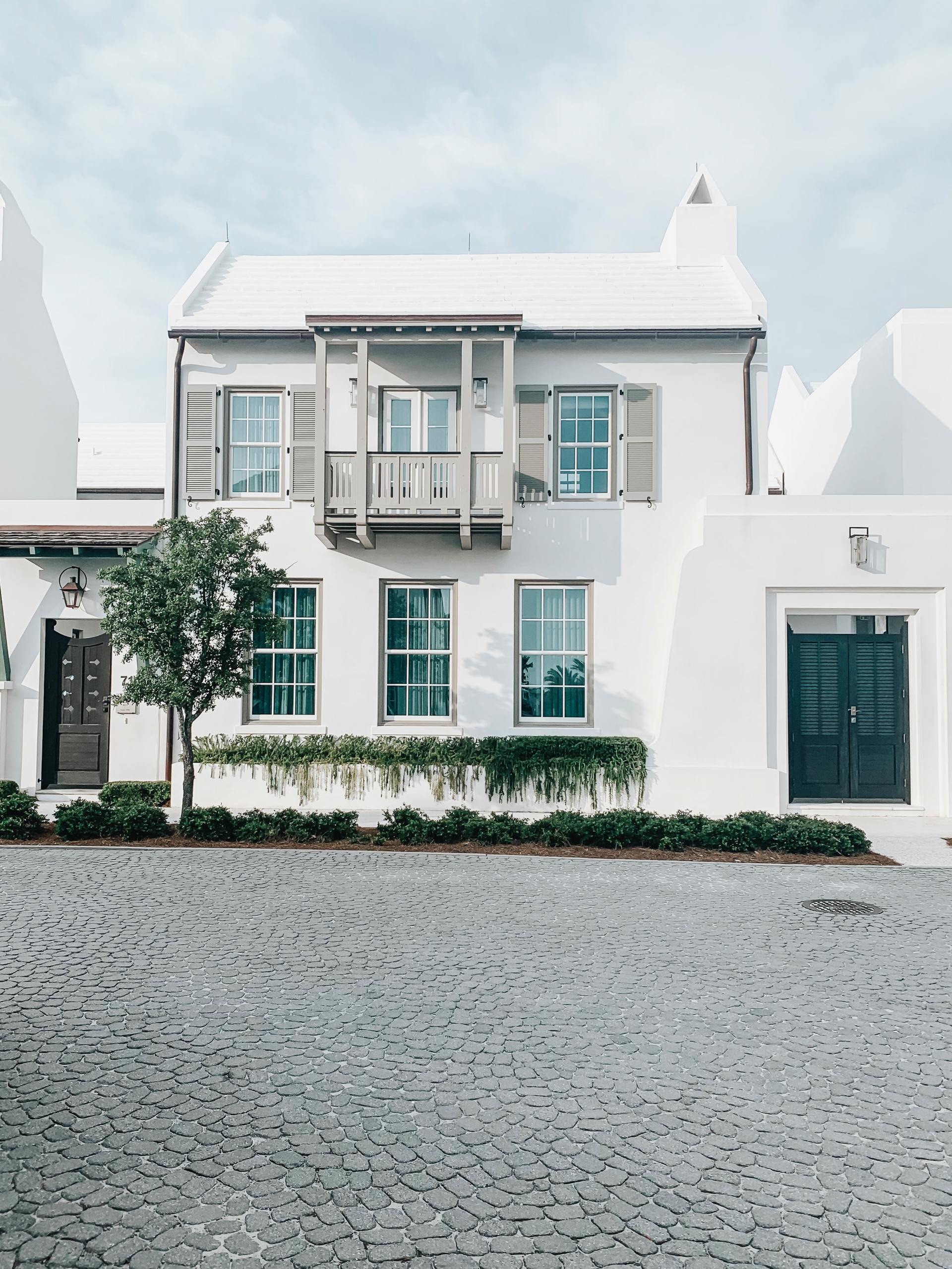 A white house with a black garage door is sitting on top of a cobblestone driveway.