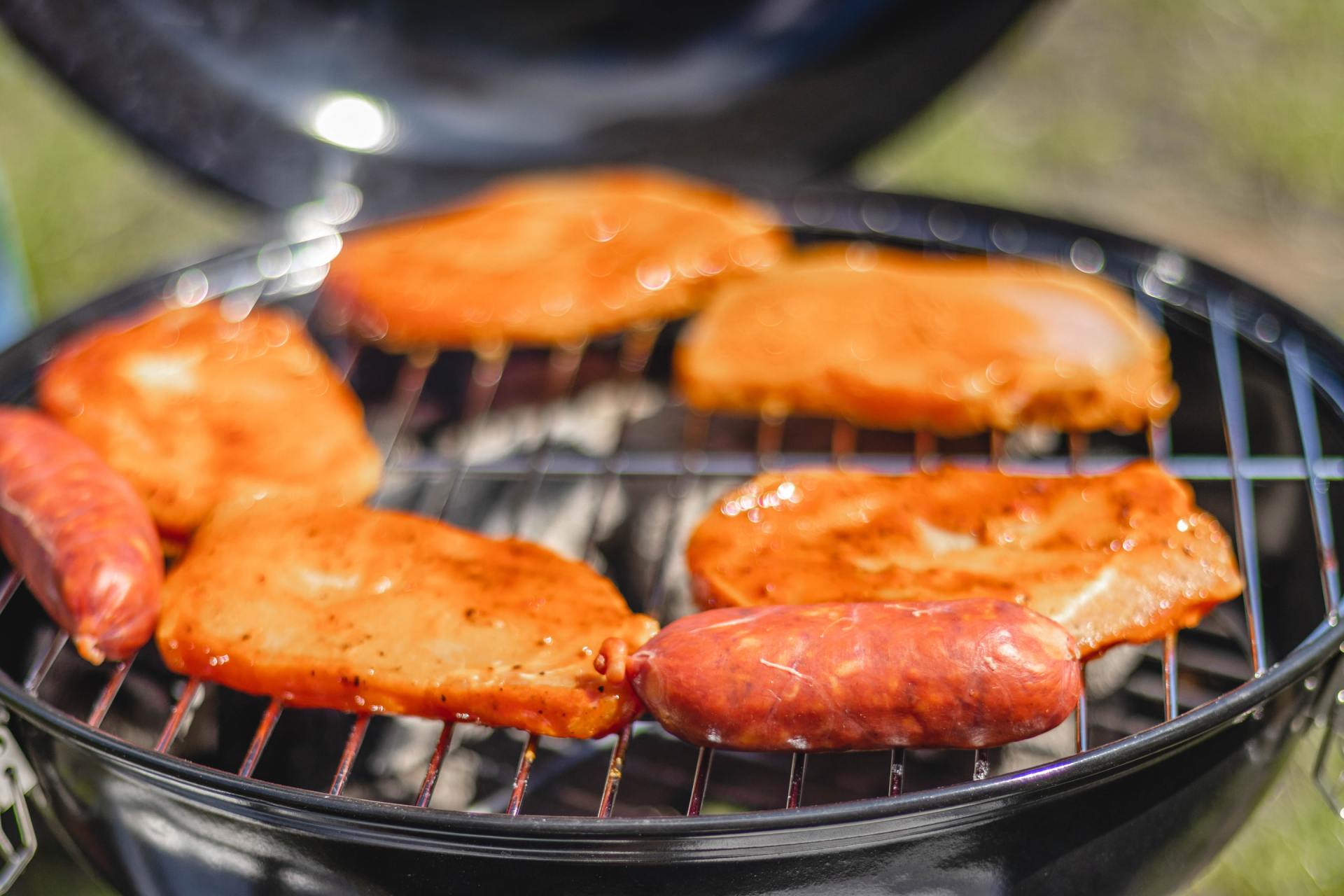 Chicken and sausages are cooking on a grill.