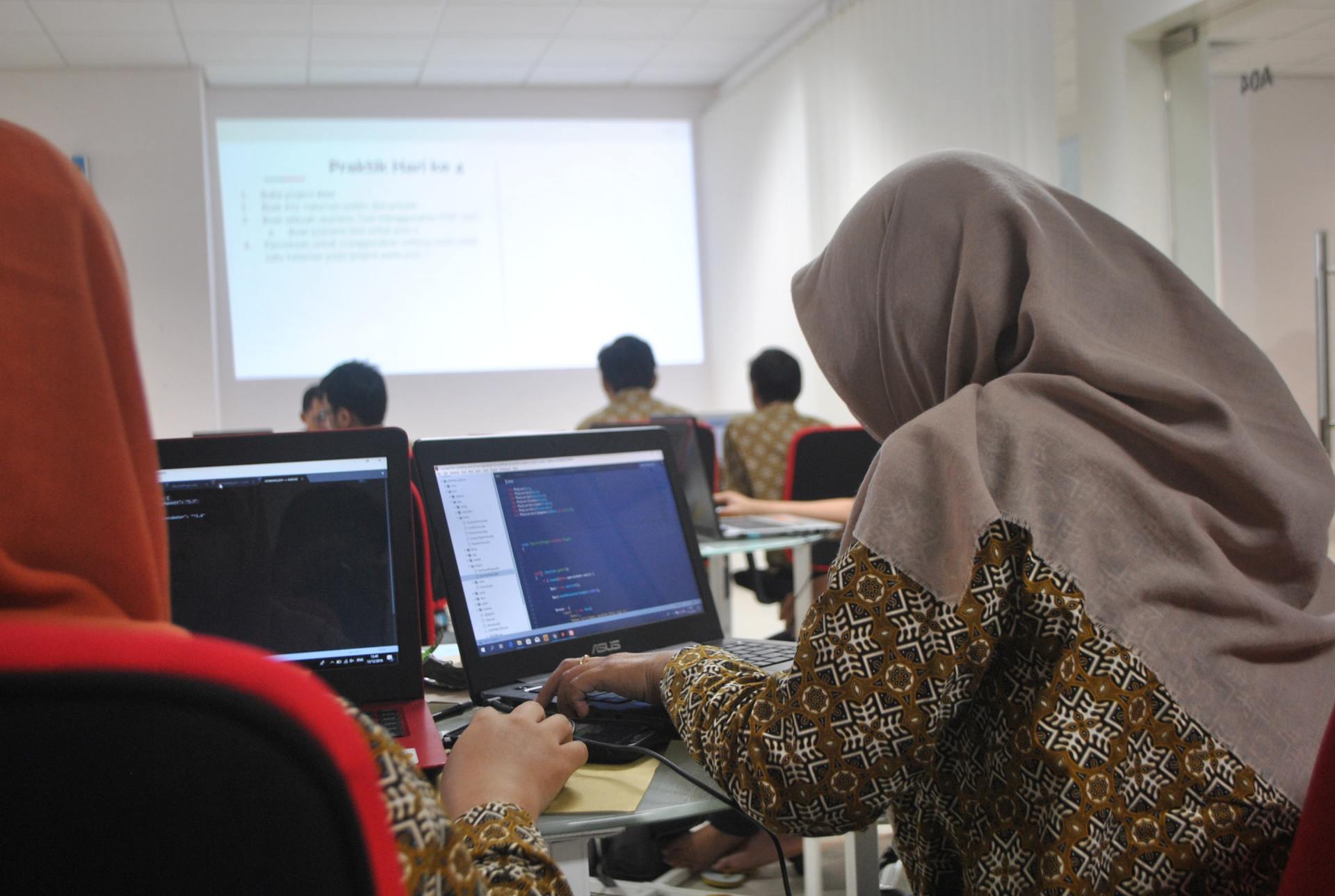 A woman in a hijab is sitting in front of a laptop computer