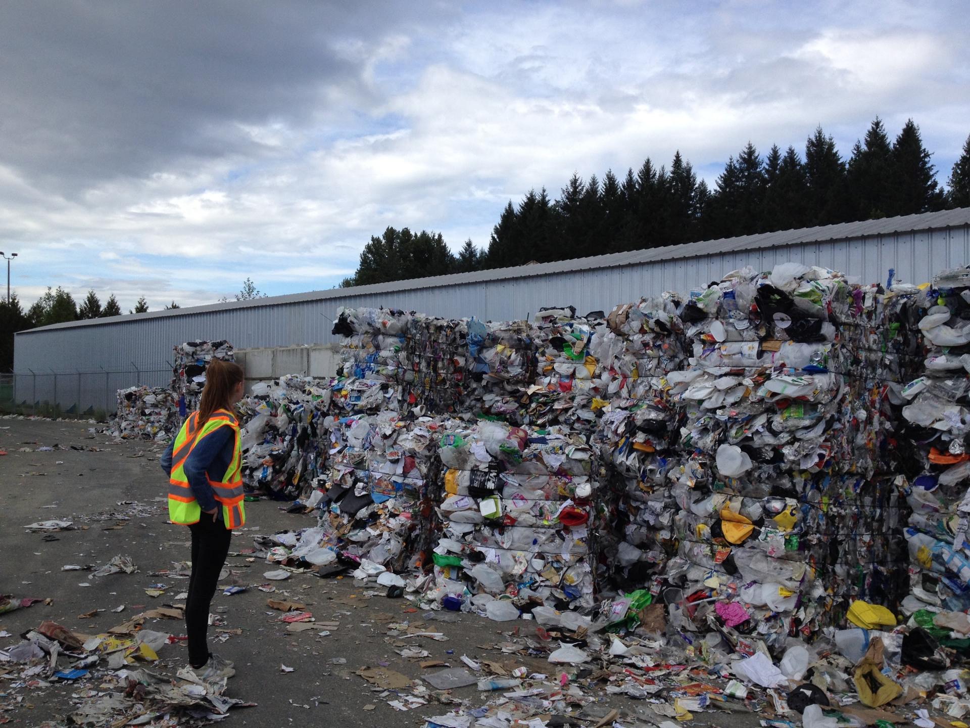 A woman is standing in front of a large pile of trash.