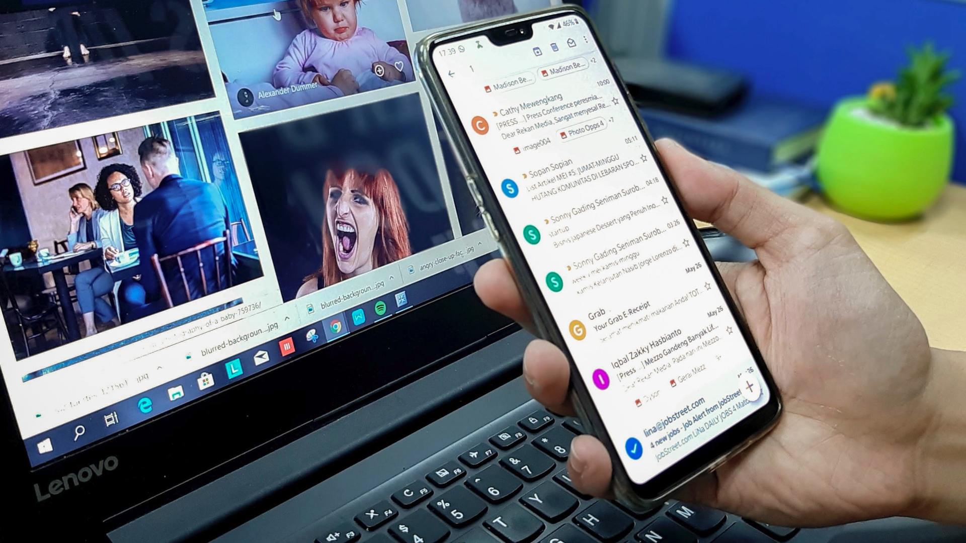 A person is holding a cell phone in front of a laptop computer.
