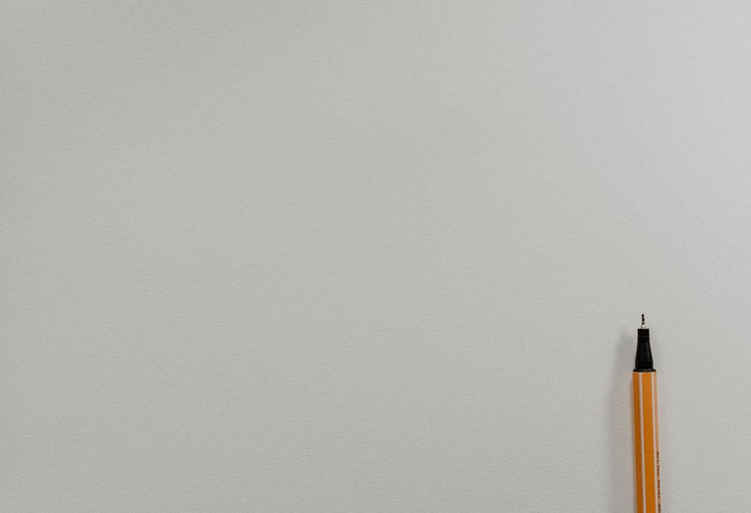 Blank light gray wall with the tip of an orange pencil at the bottom right edge