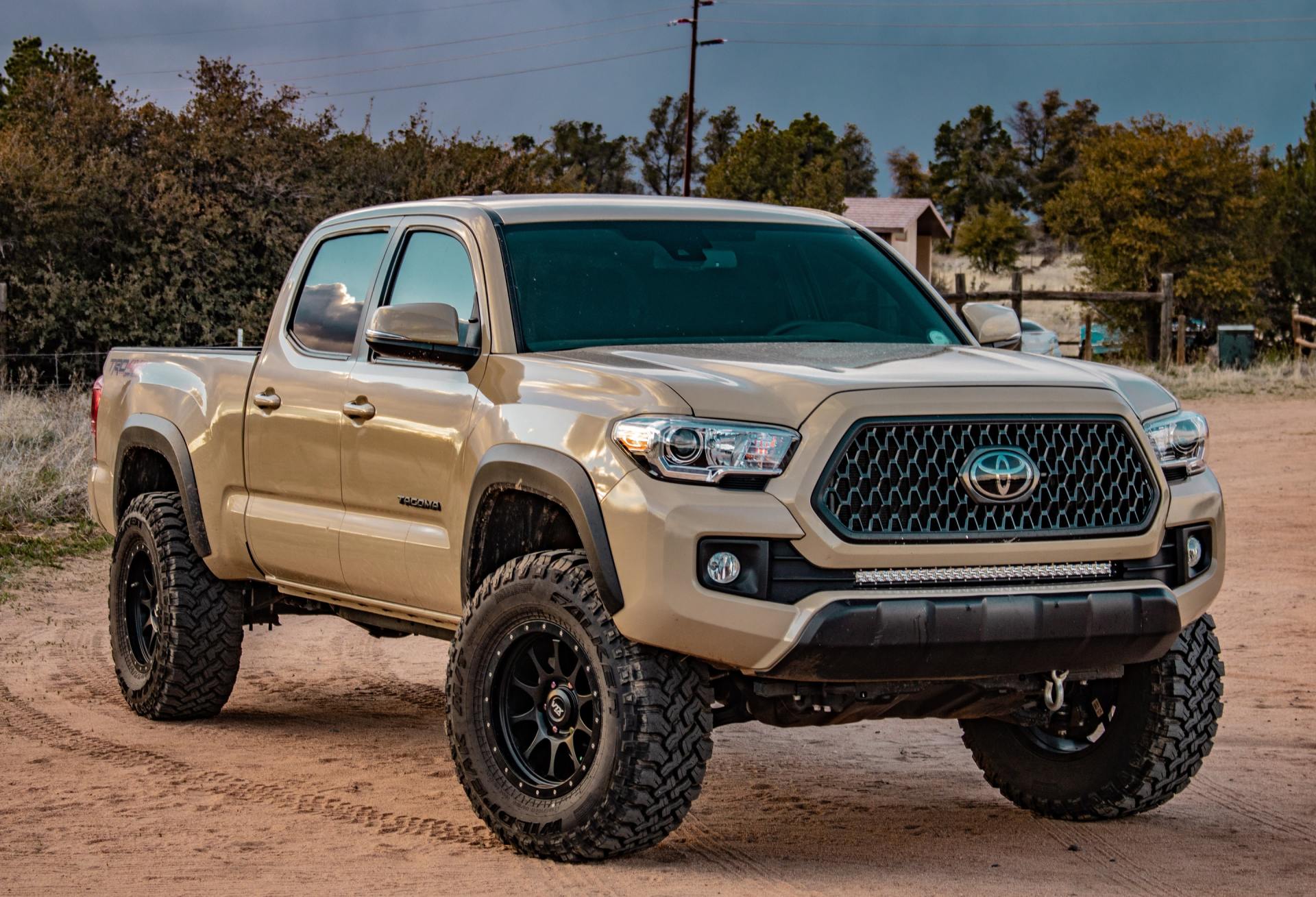 A tan toyota tacoma truck is parked in a dirt field.