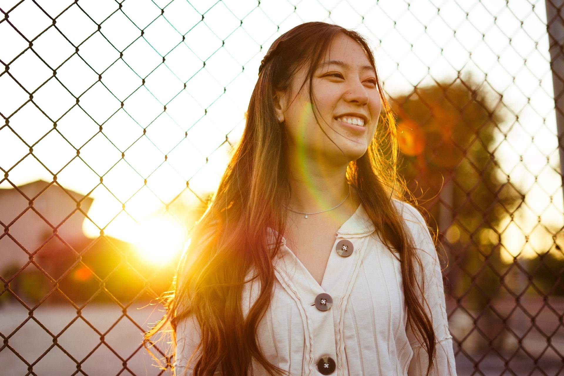 A woman is smiling while standing in front of a chain link fence.