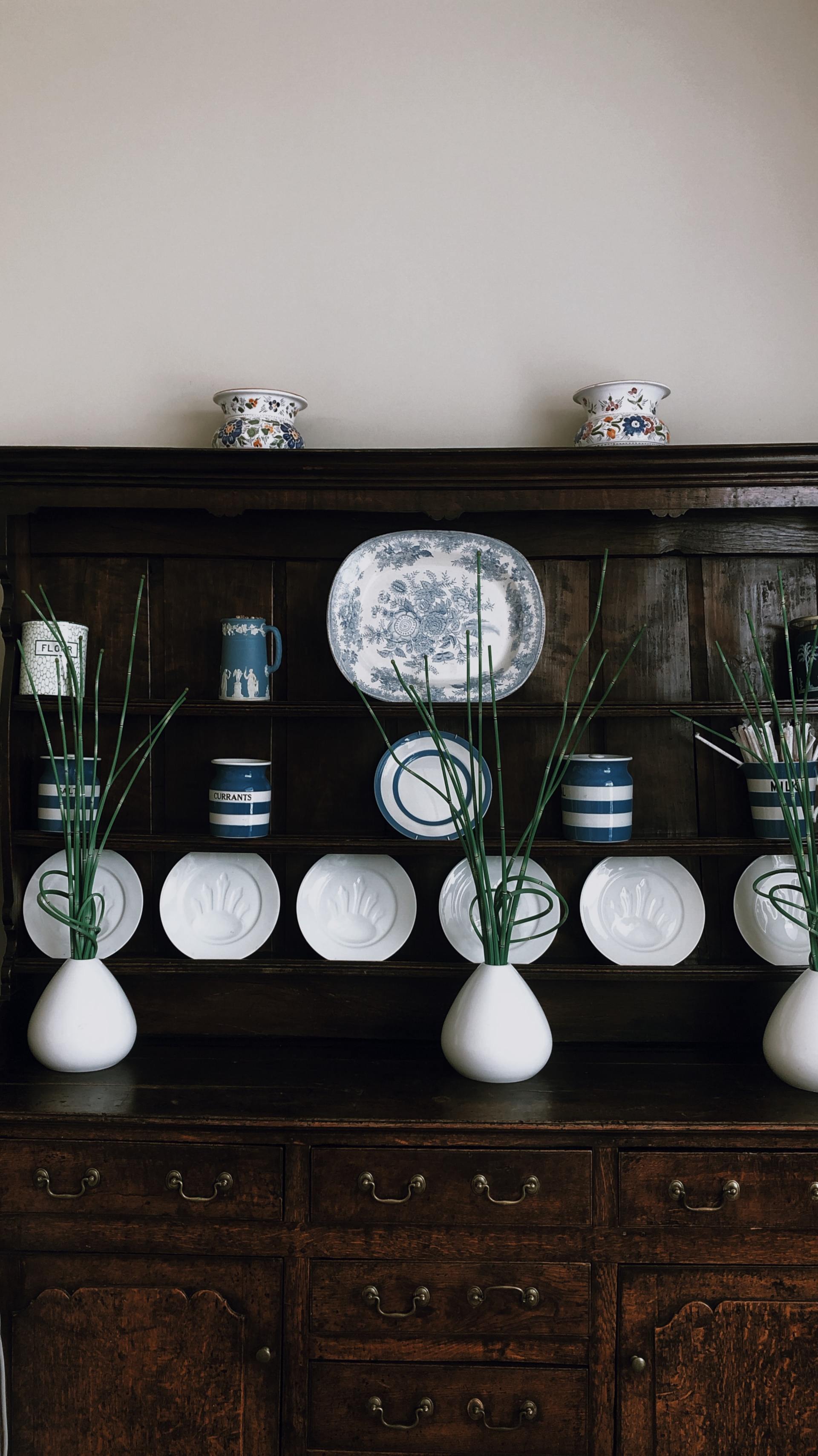 Wooden hutch displaying white and blue china with vases of green foliage.