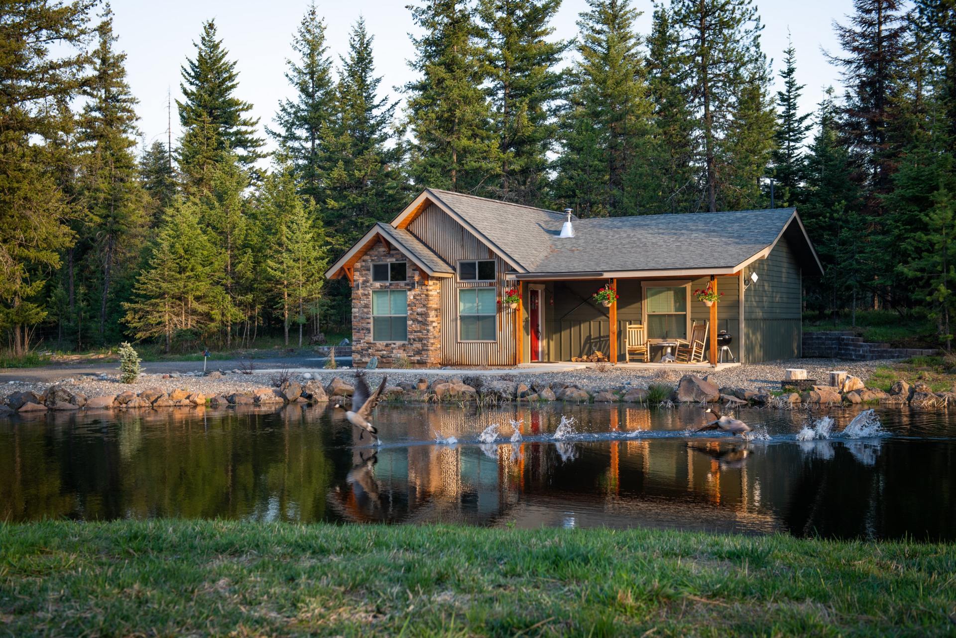 A house is sitting next to a lake in the middle of a forest.