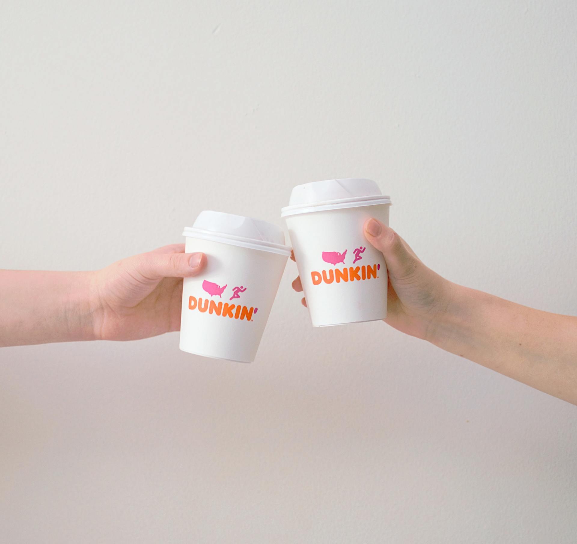 Two people are toasting with dunkin ' donuts cups.