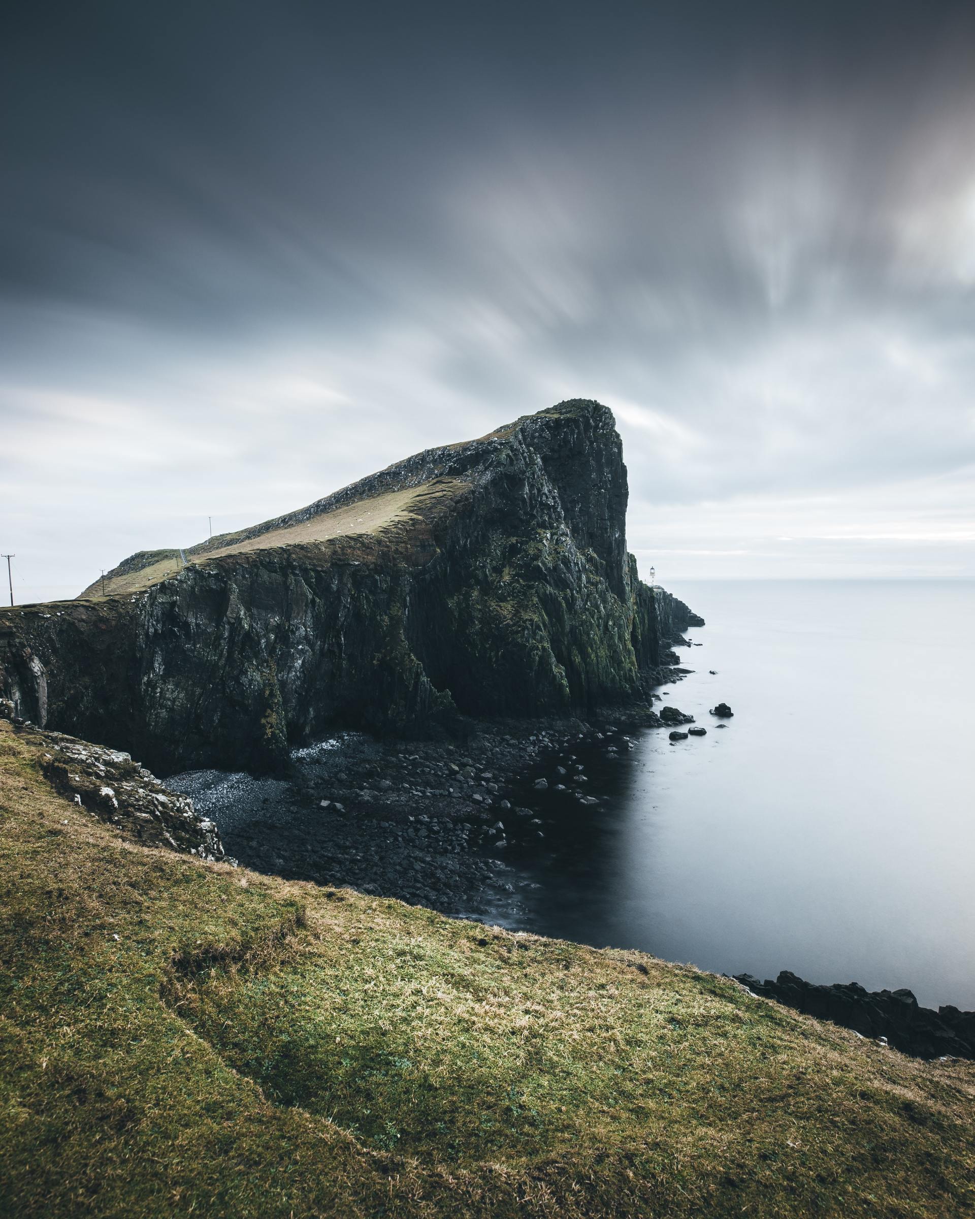 Rocky cliffside jutting into calm sea under a cloudy sky.