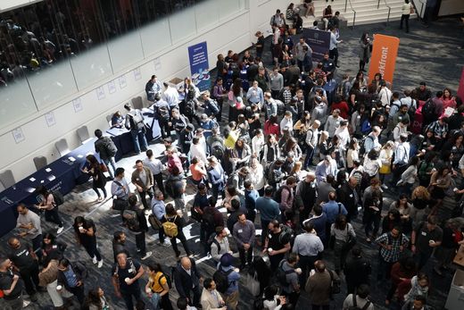 Crowded indoor event hall with many people mingling near booths and banners