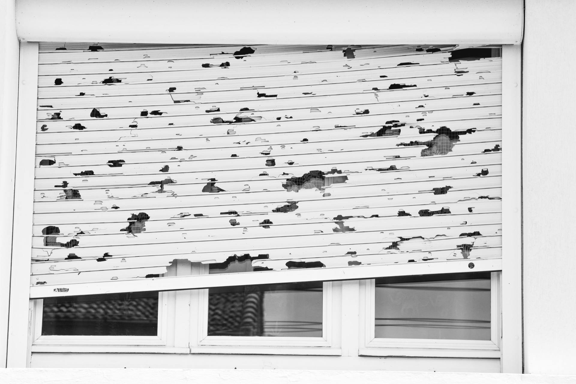 White window with damaged, partially closed shutter.