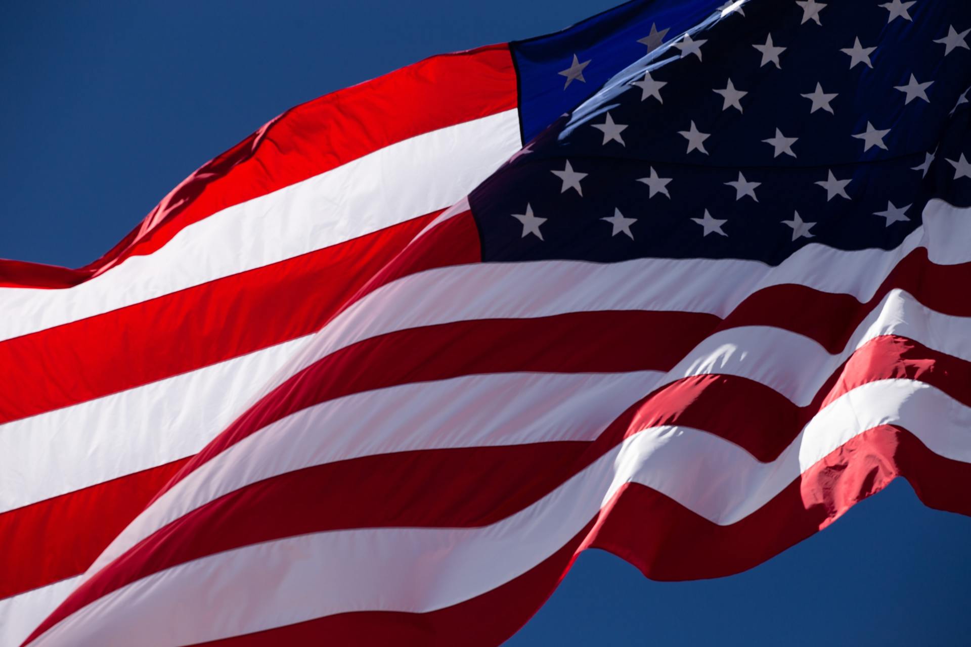 American flag waving in front of a blue sky, red and white stripes, stars in a blue field.