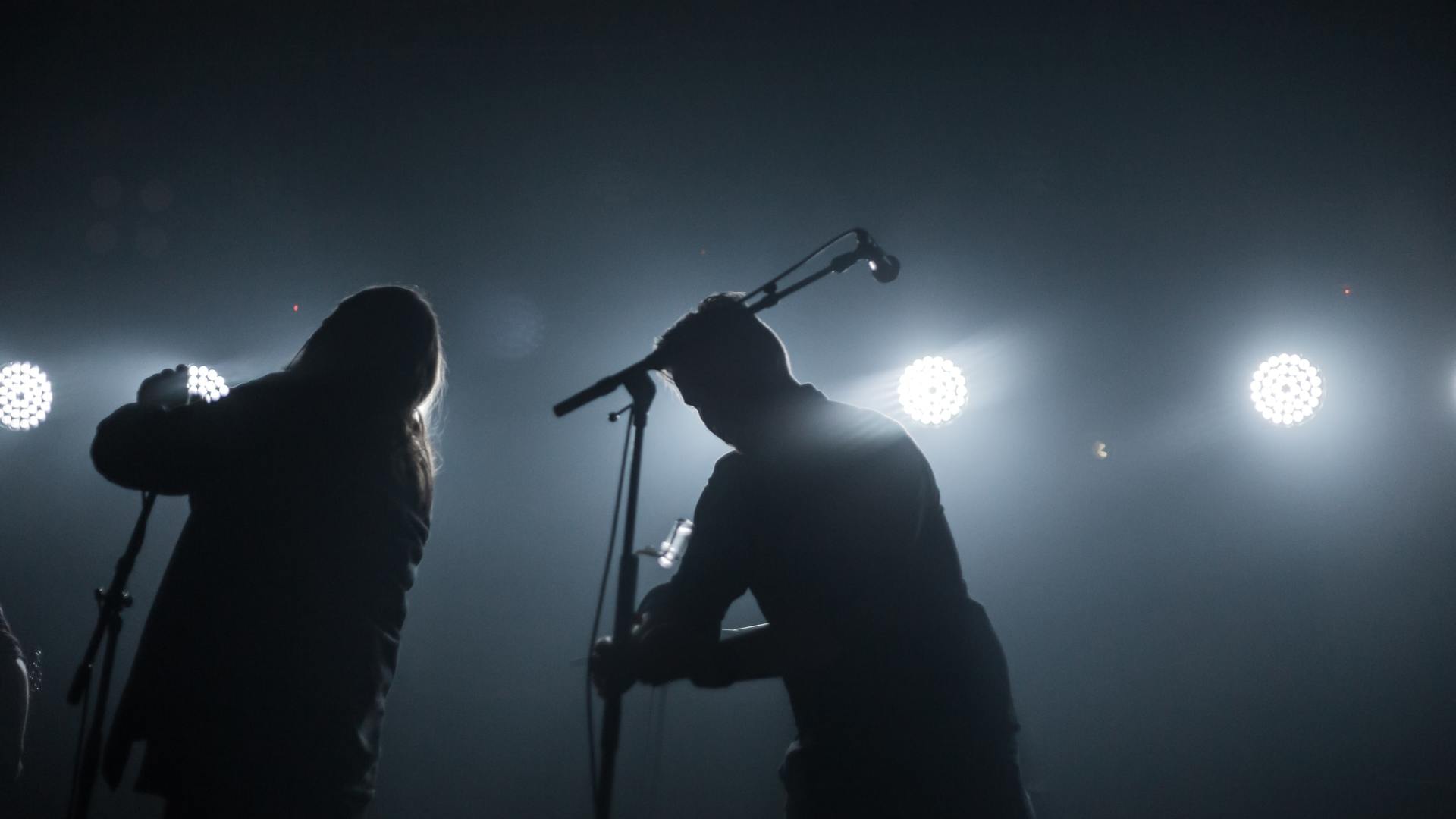 Two silhouetted musicians performing on a foggy stage with bright backlights