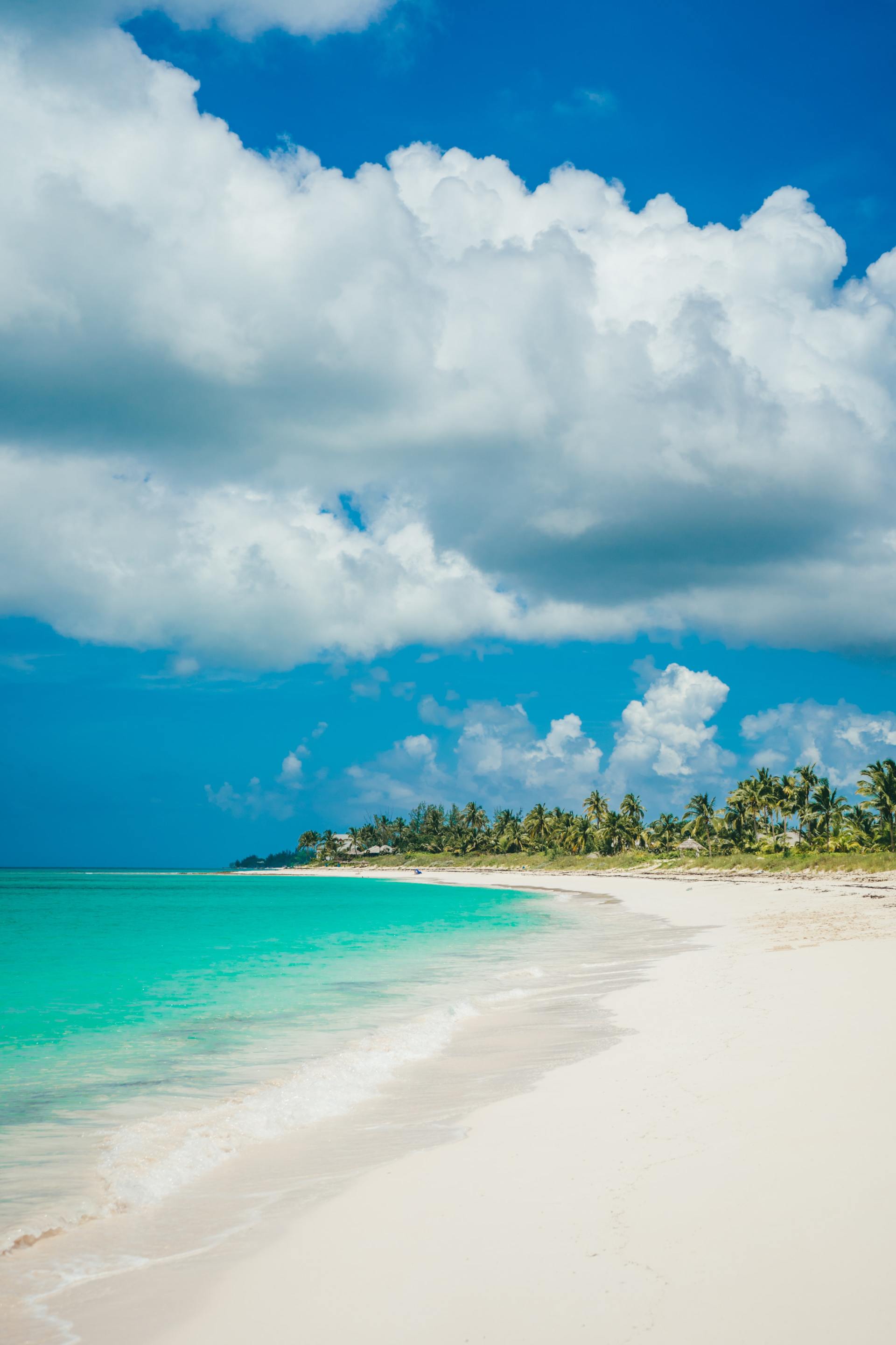 White sandy beach with turquoise water under a blue sky dotted with puffy white clouds.
