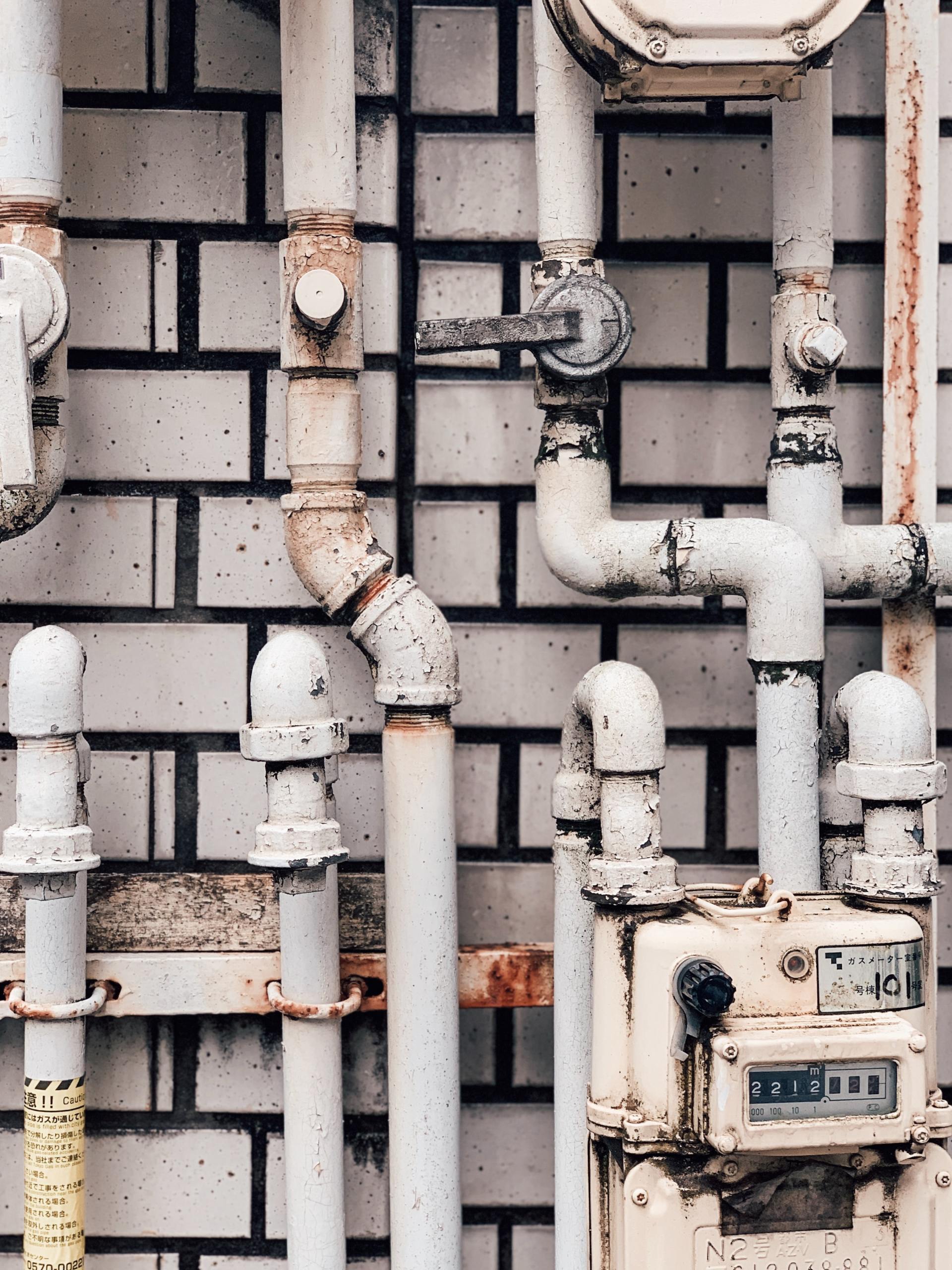 A brick wall with white pipes and a gas meter