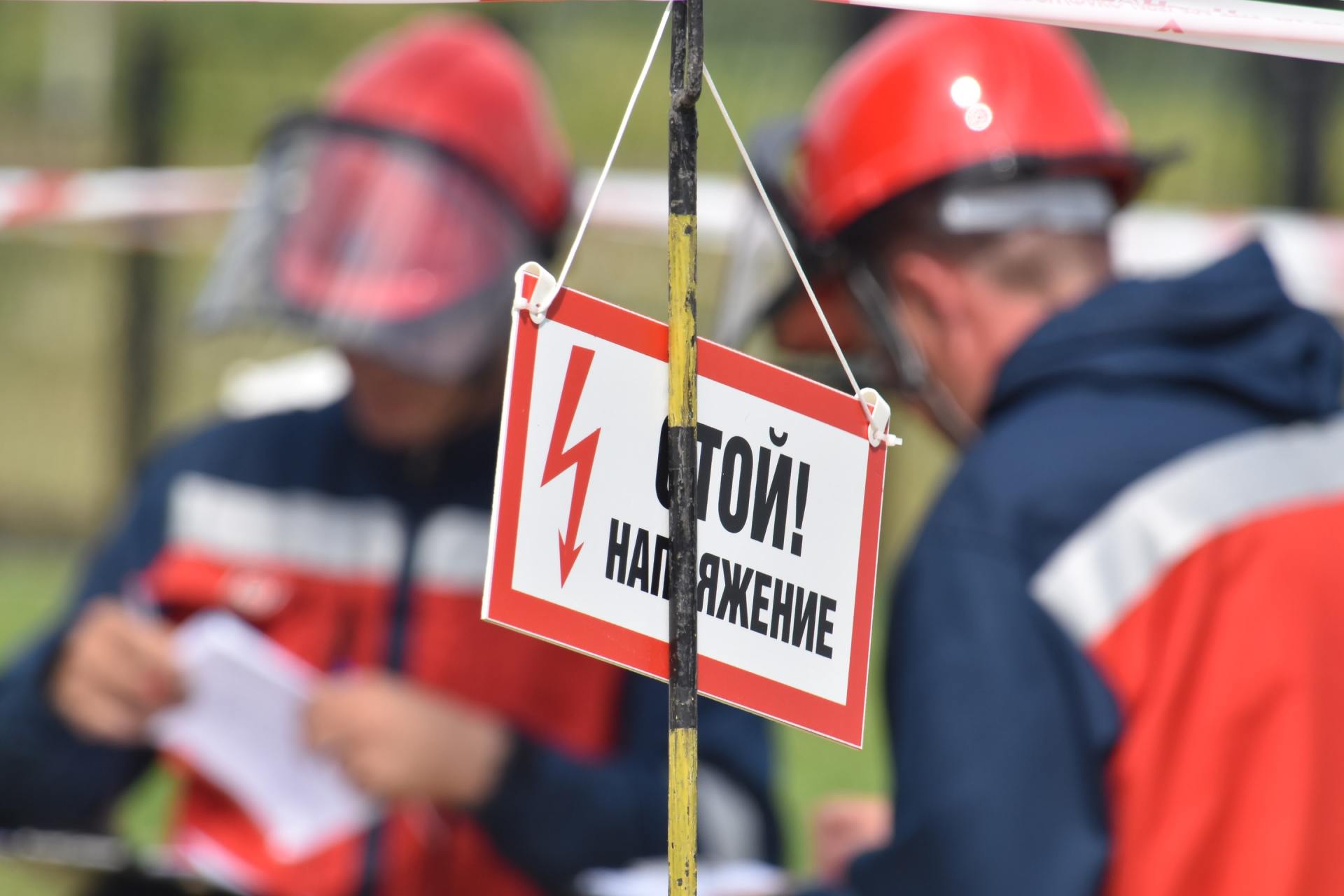 Zwei Feuerwehrleute in roten Helmen inspizieren ein Warnschild, das draußen an einem Seil hängt.