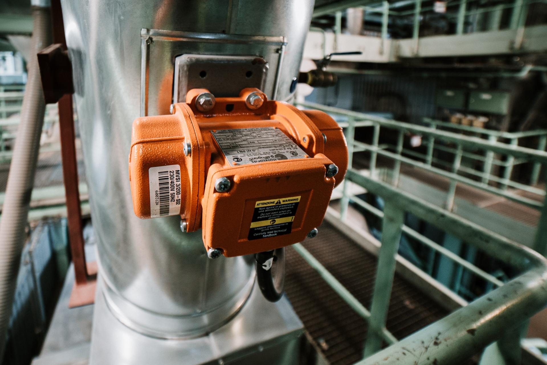 A close up of an orange device on a metal pipe in a factory.