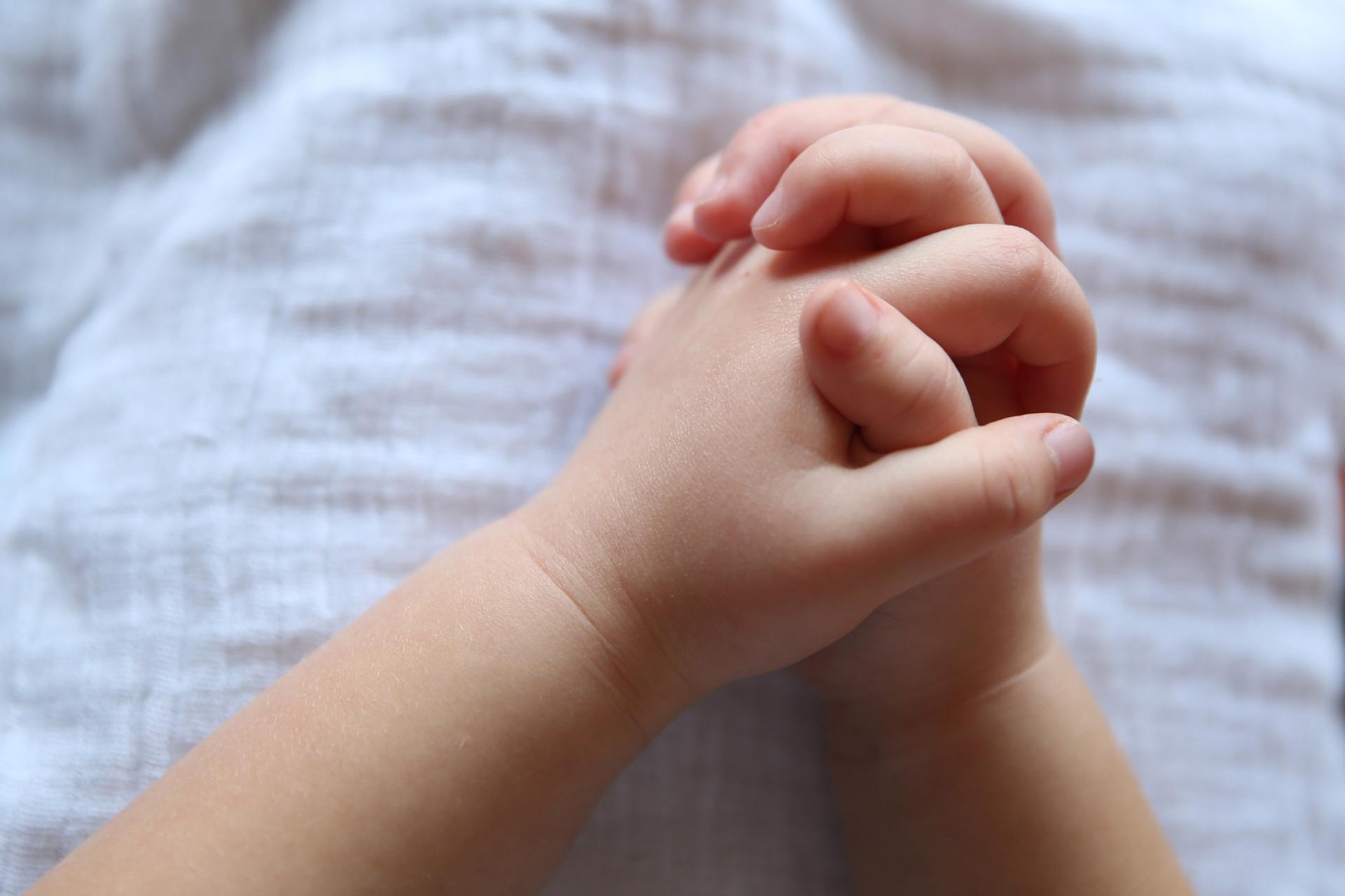 A baby 's hands are folded in prayer on a bed.