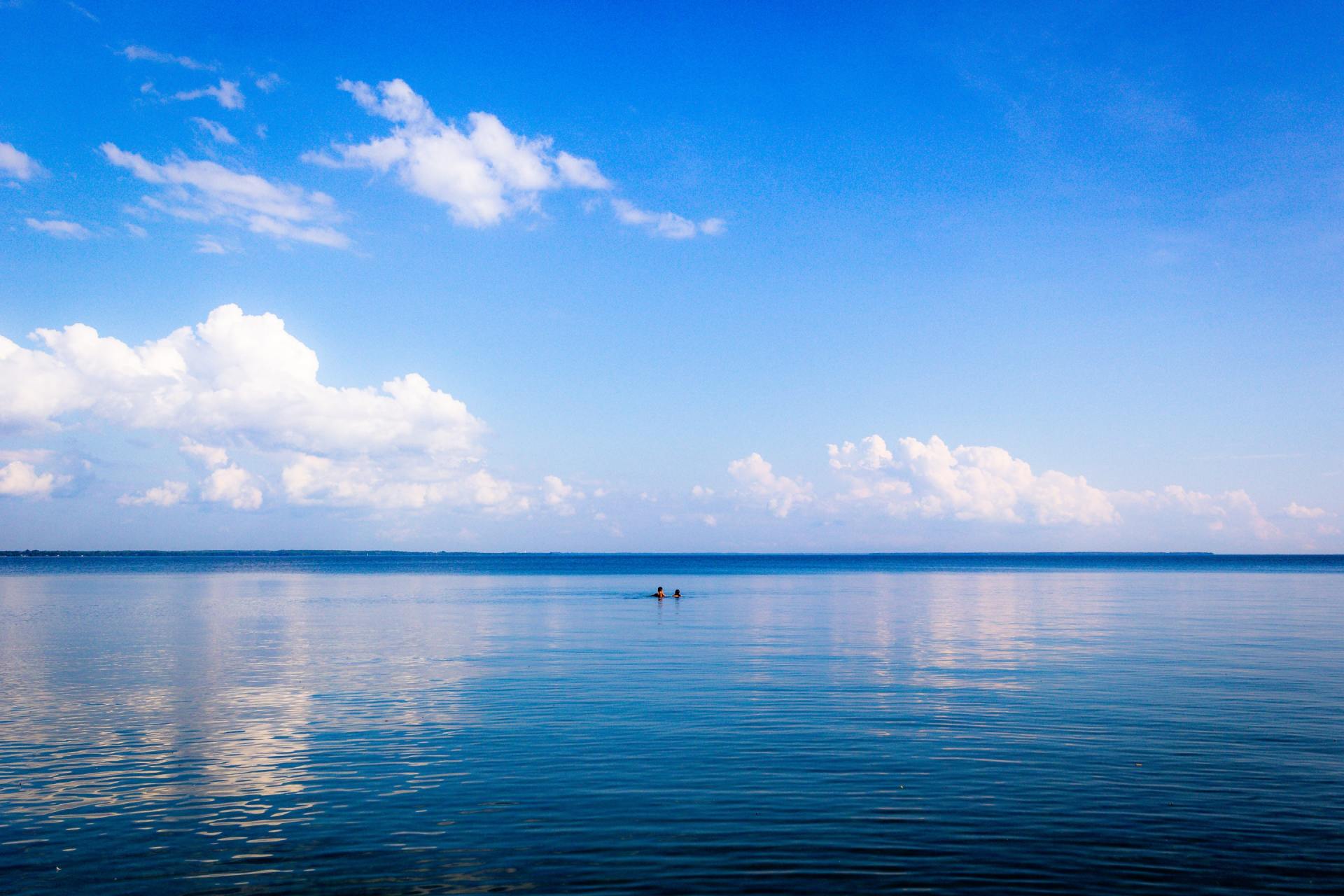 Een kalme blauwe oceaan onder een helderblauwe hemel met hier en daar witte wolken.