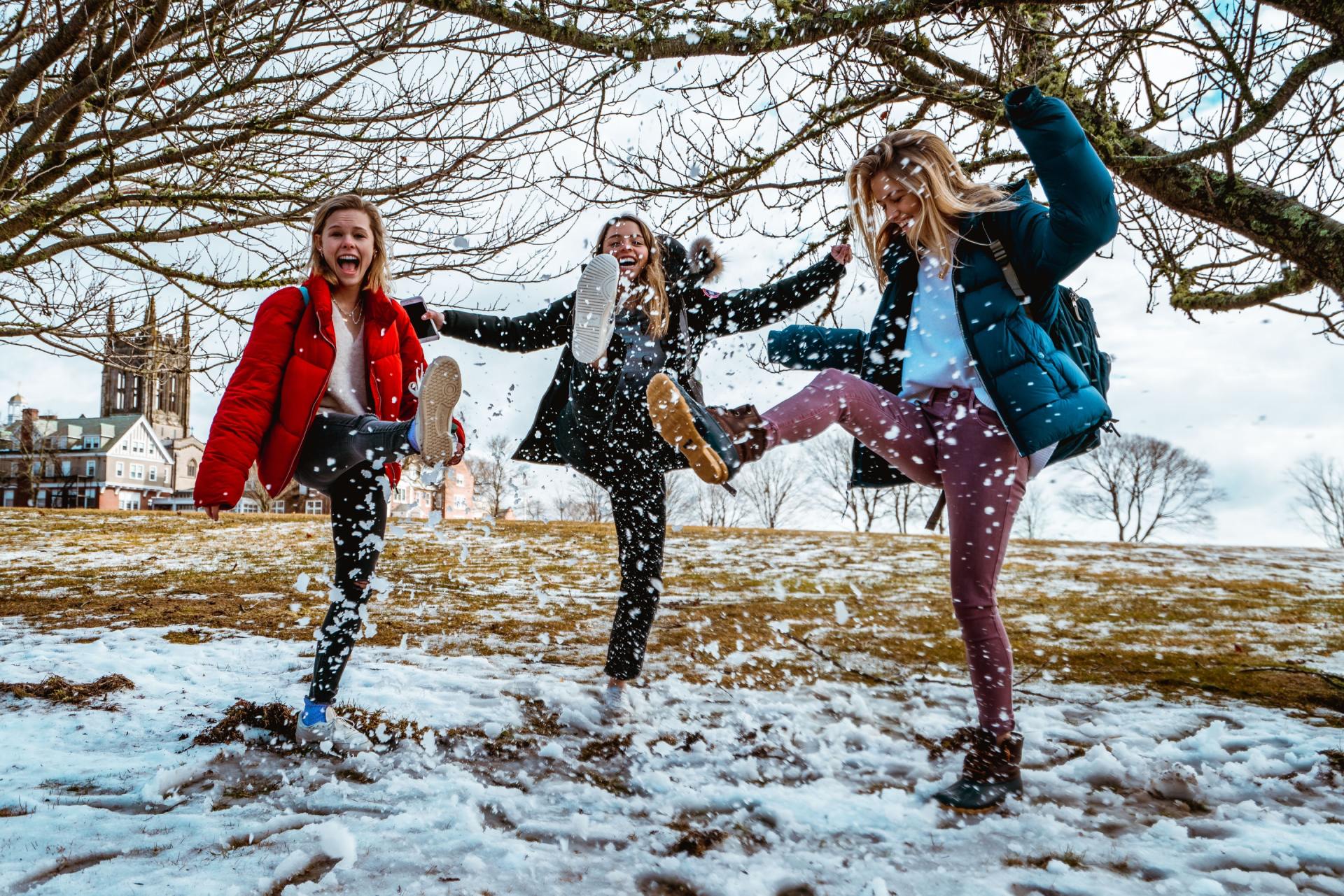 Three women are playing in the snow with their feet in the air.