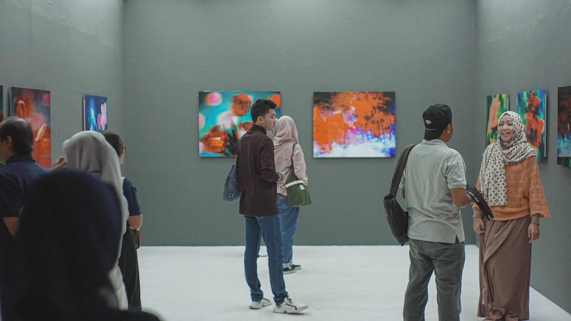 People viewing abstract art in a gallery; gray walls, diverse group, observing colorful paintings.