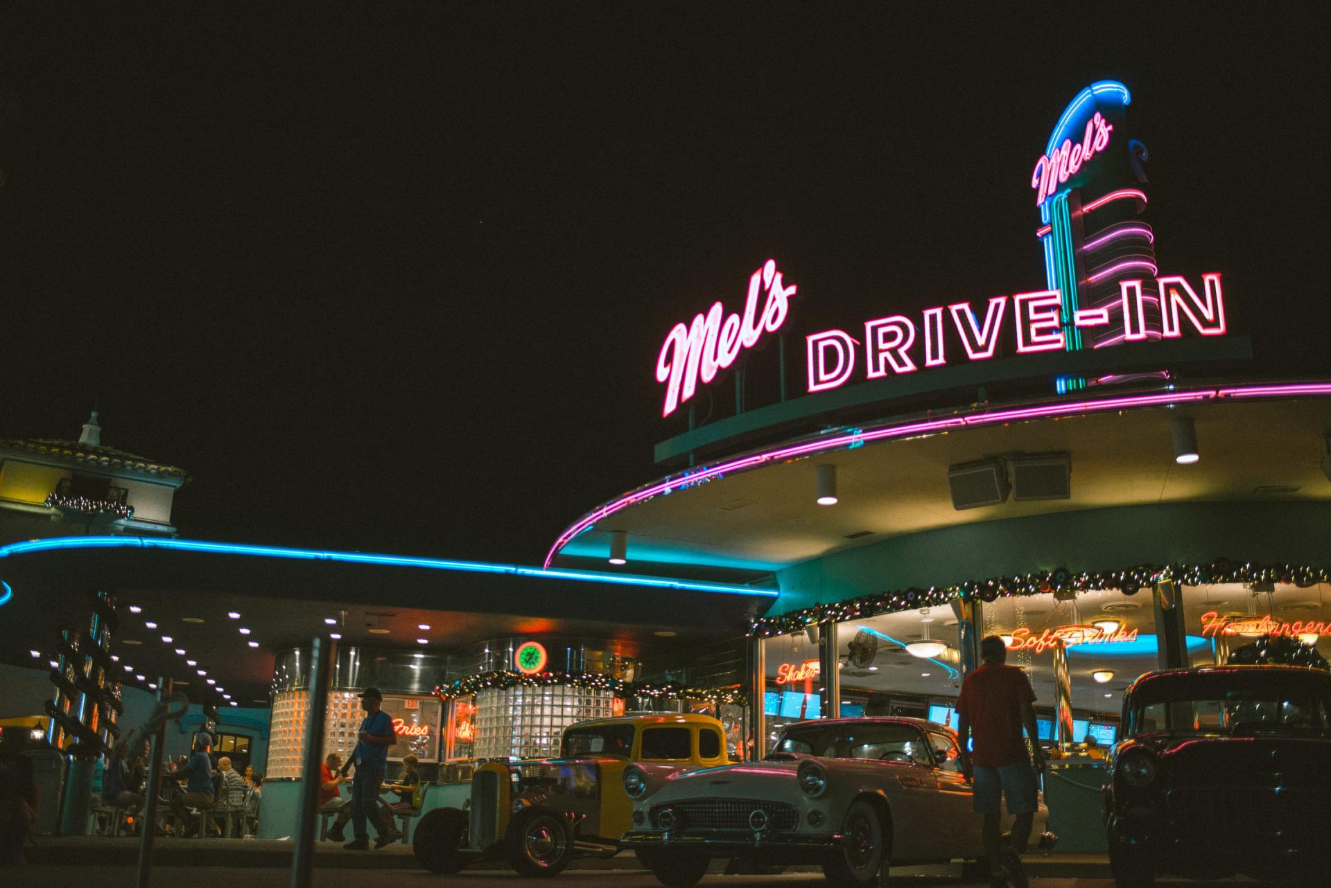A man is standing in front of a drive-in restaurant at night.